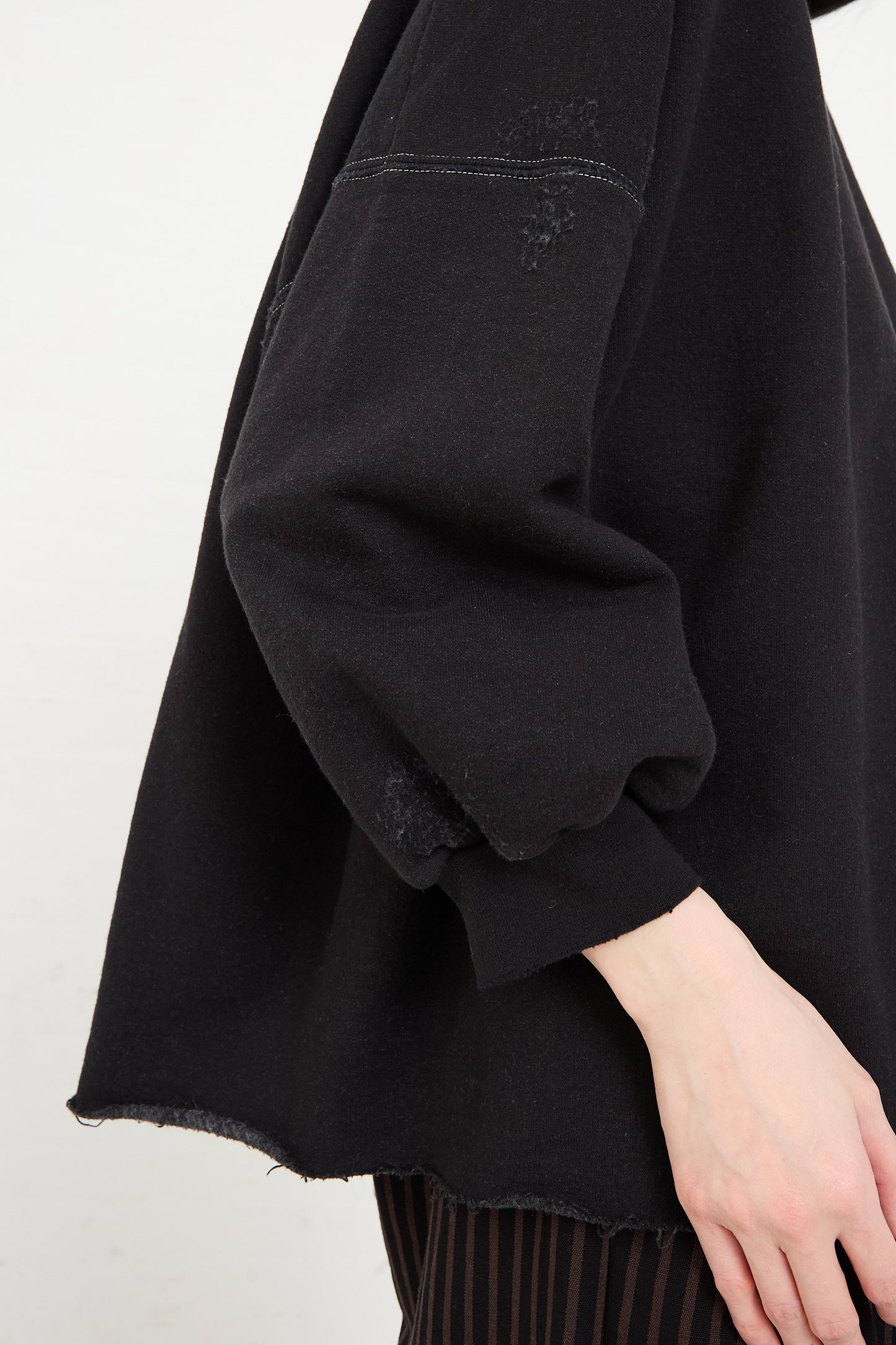 Close-up of a person in a genderless Fond Sweatshirt in Charcoal by Rachel Comey with a frayed hem.