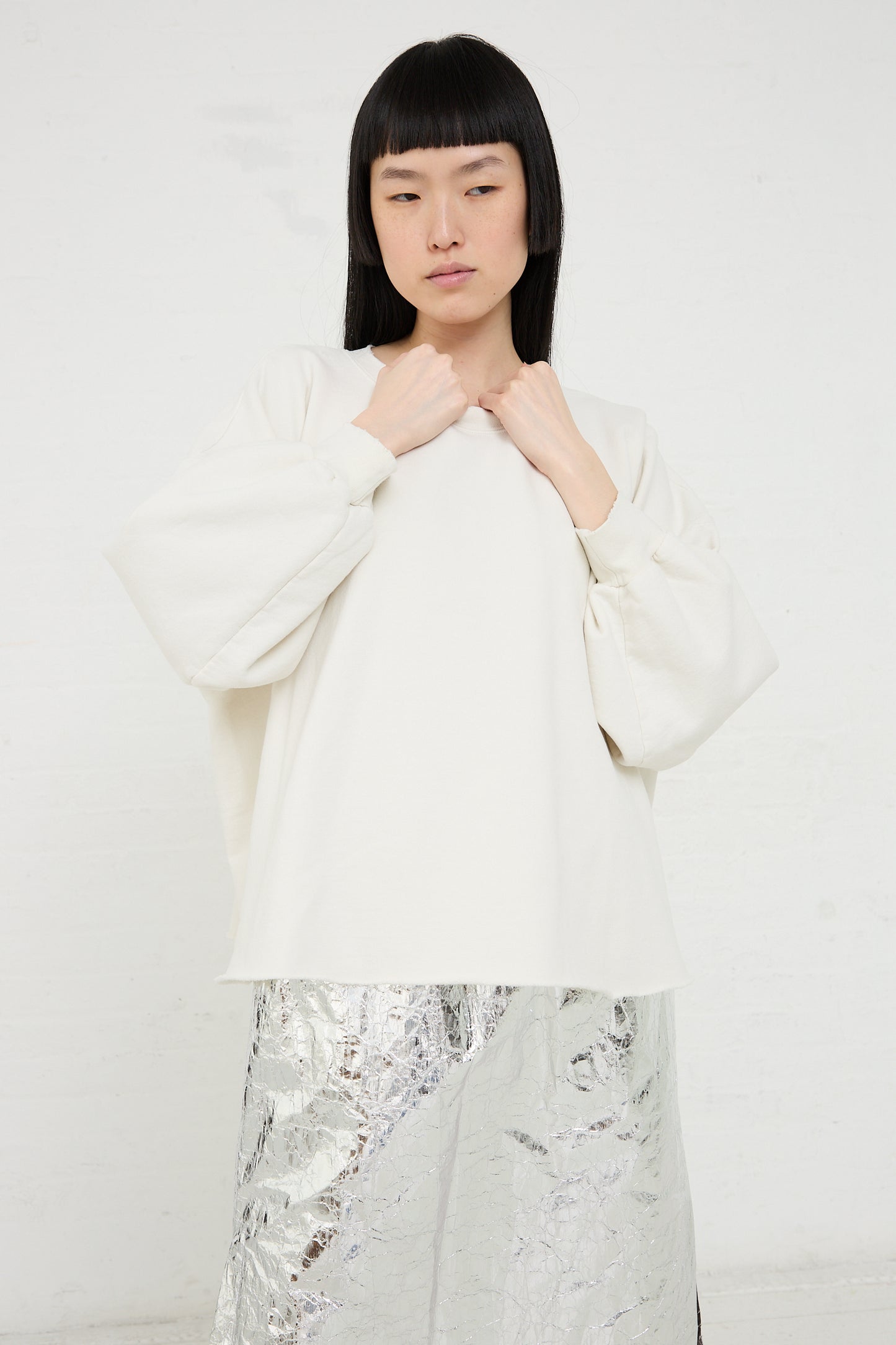 Woman posing in a Rachel Comey Fond Sweatshirt in Dirty White and metallic silver skirt against a white background.