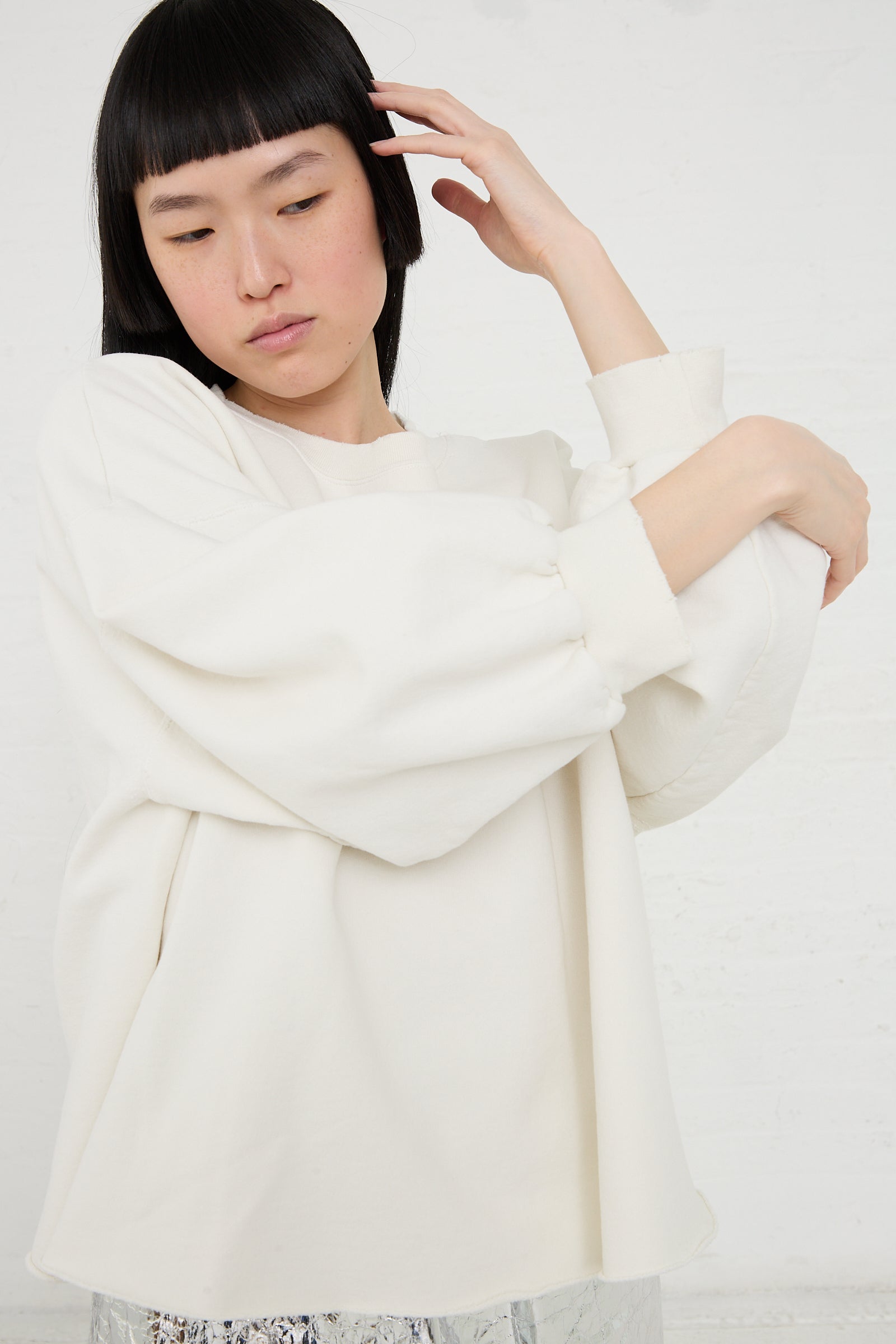 Individual in a Rachel Comey Fond Sweatshirt in Dirty White, oversized sweatshirt posing with their hand on their head.