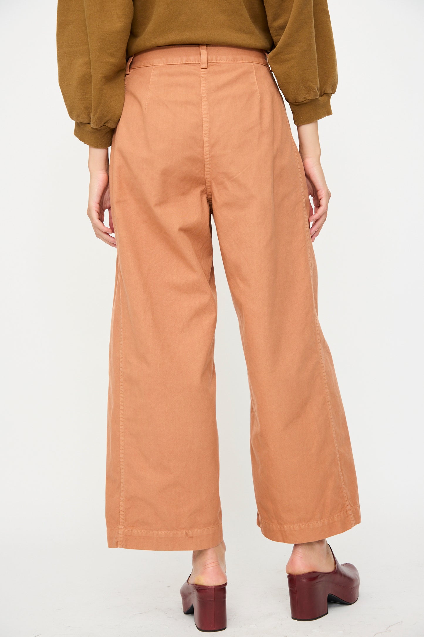 Person shown from the back wearing Rachel Comey's Garra Pant in Copper, a wide-leg, high-waisted jean, paired with brown heeled shoes against a plain white background.