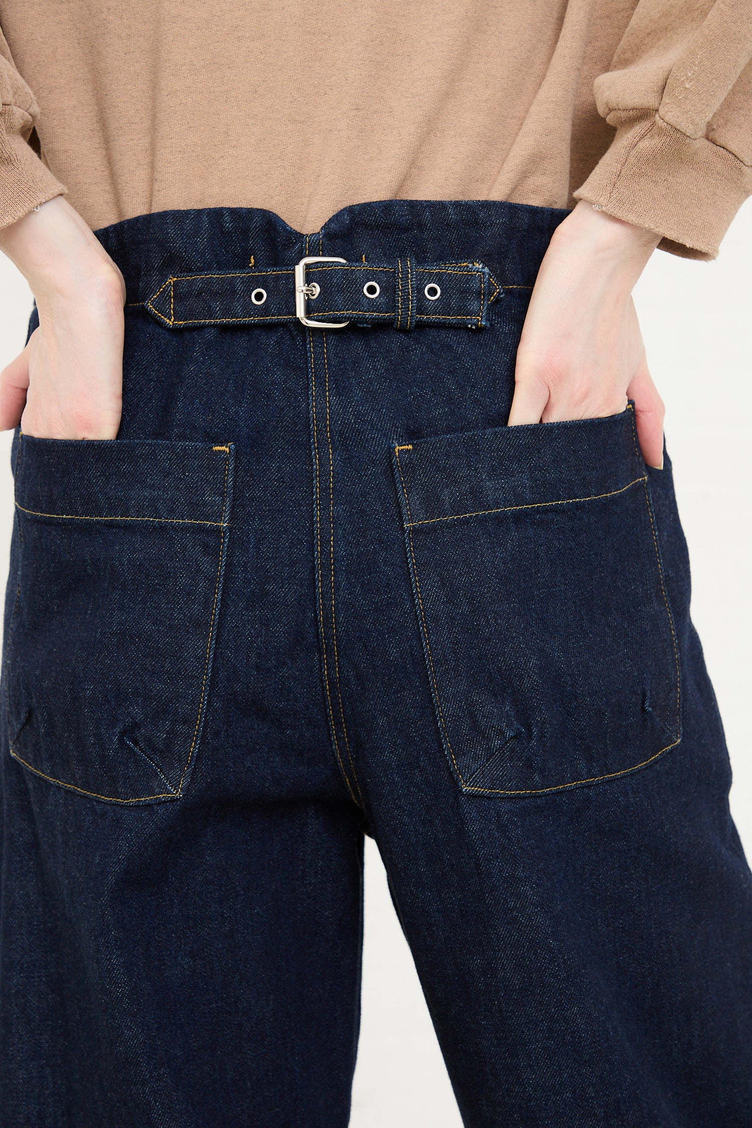 A close-up of a person wearing Rachel Comey's Handy Pant in Dark Indigo denim jeans with hands casually placed in the back pockets.