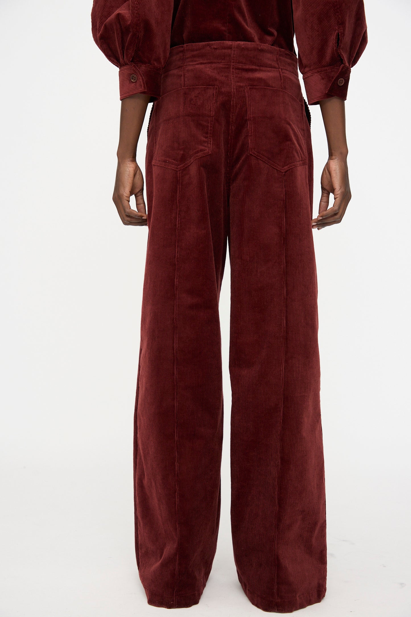 A person is shown from the back wearing Rachel Comey's Lanett Cord Pant in Brick, a high-waisted, wide-leg corduroy style paired with a matching long-sleeve top against a white background—ideal for lovers of women’s relaxed-fit retro pants.