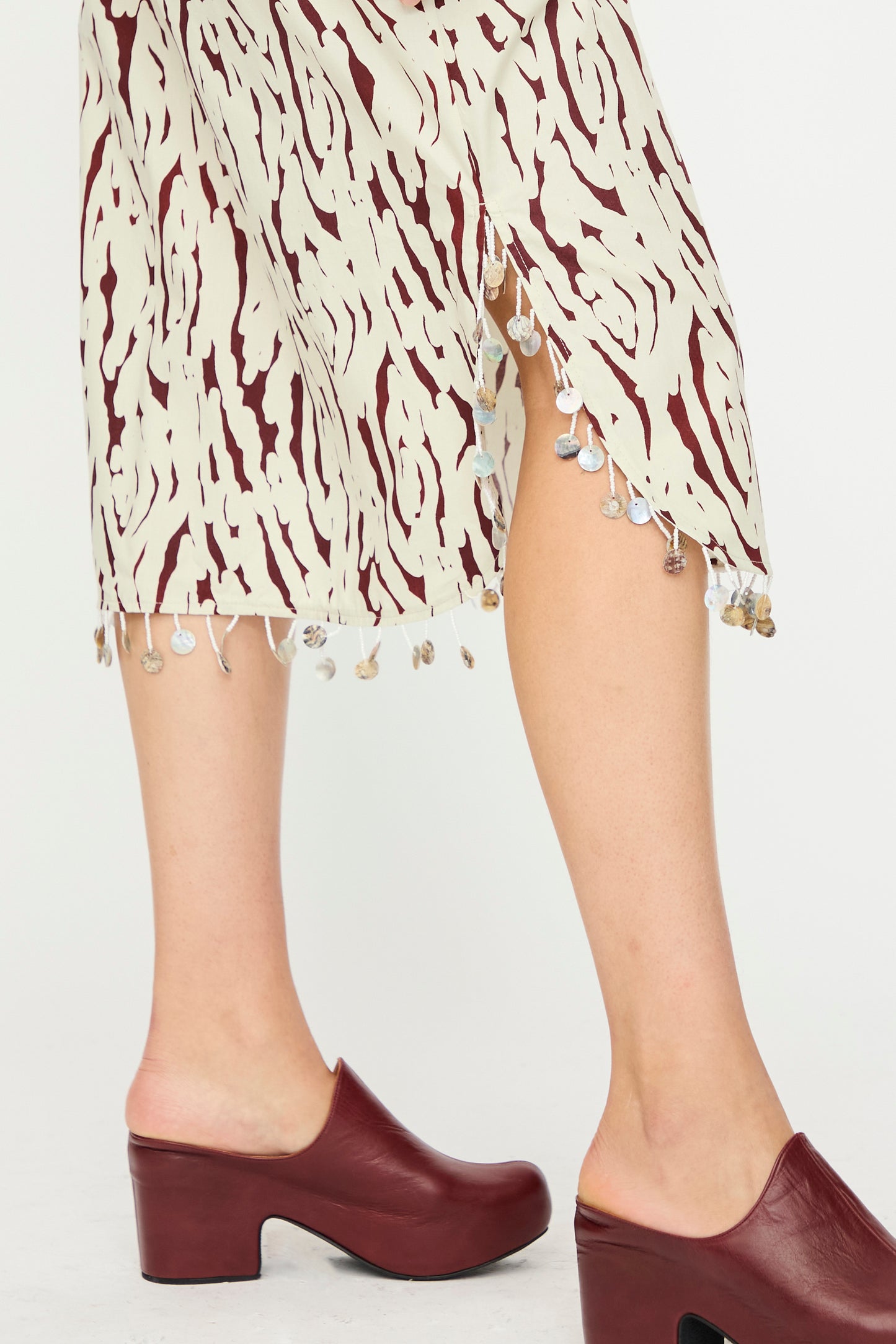 A person wearing the Rachel Comey Lastica Skirt in Cream—an abstract printed cotton midi skirt with sequin trim—paired with burgundy block-heeled clogs.