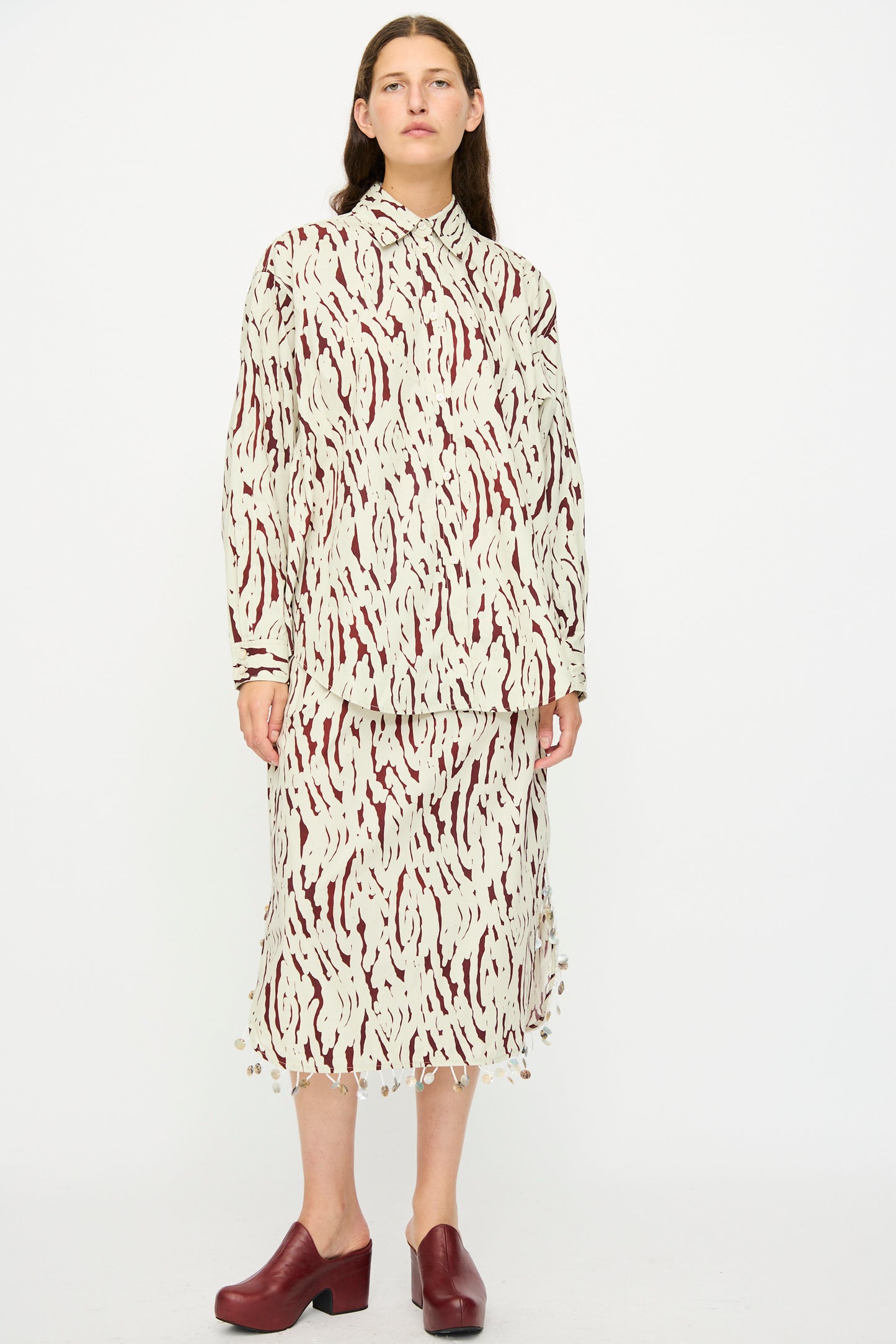 A person wears the Rachel Comey Lastica Skirt in Cream with a matching abstract pattern shirt and maroon closed-toe shoes, standing against a white background.