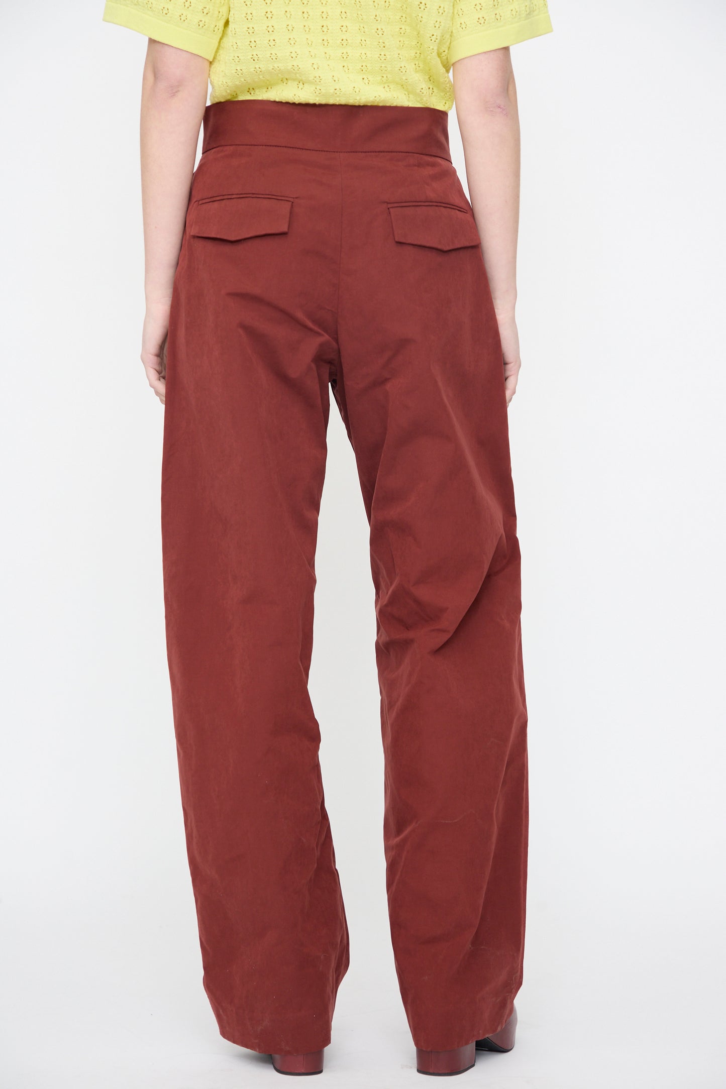 Person wearing the Rachel Comey Lyson Pant in Garnet, a high-waisted, water-repellent wide leg brown pant with back flap pockets, paired with a yellow short-sleeve top, shown from the rear.