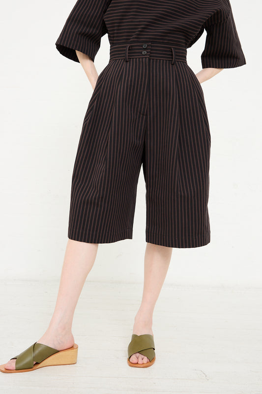 Woman wearing a pinstriped jumpsuit with wide-legged Bermuda Melio Shorts in Black and olive green sandals by Rachel Comey.