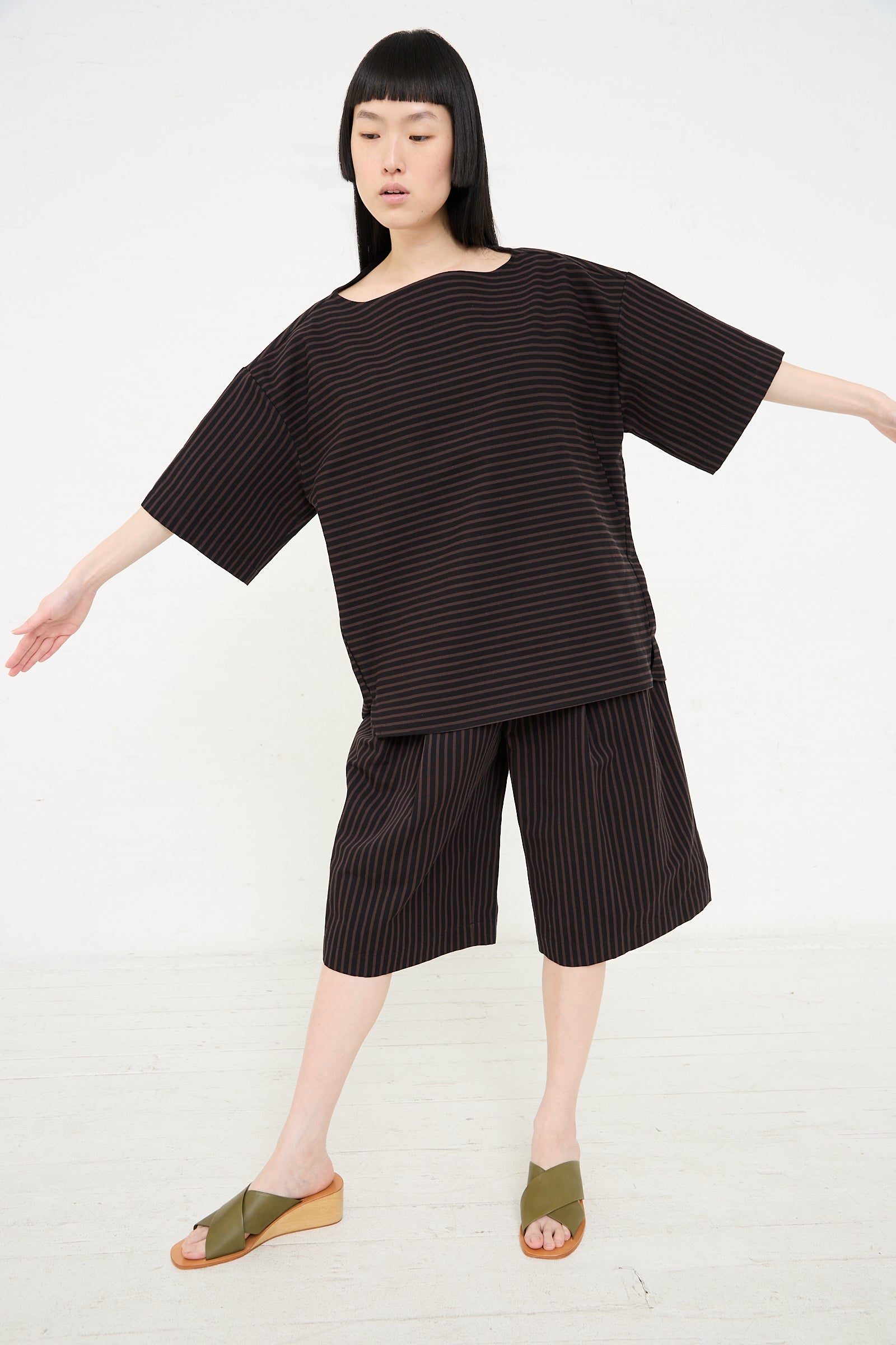 A woman in a Rachel Comey Ode Top in Black with a boatneck collar posing with arms extended.