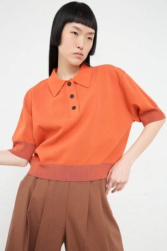 Woman in a vibrant Omin Top in Orange by Rachel Comey and brown trousers.