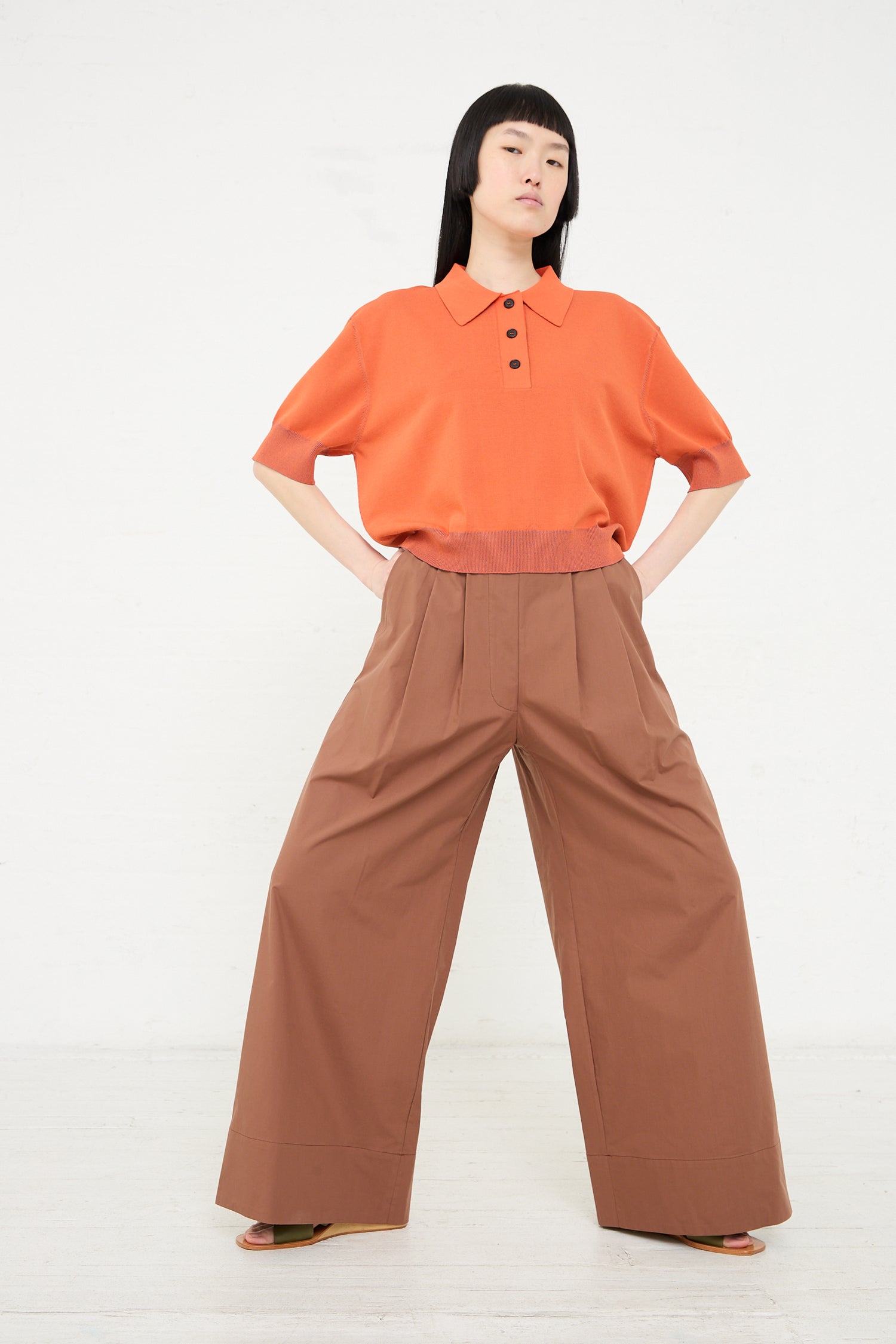 Woman posing in a studio wearing a Rachel Comey Omin Top in Orange and wide-leg brown trousers.