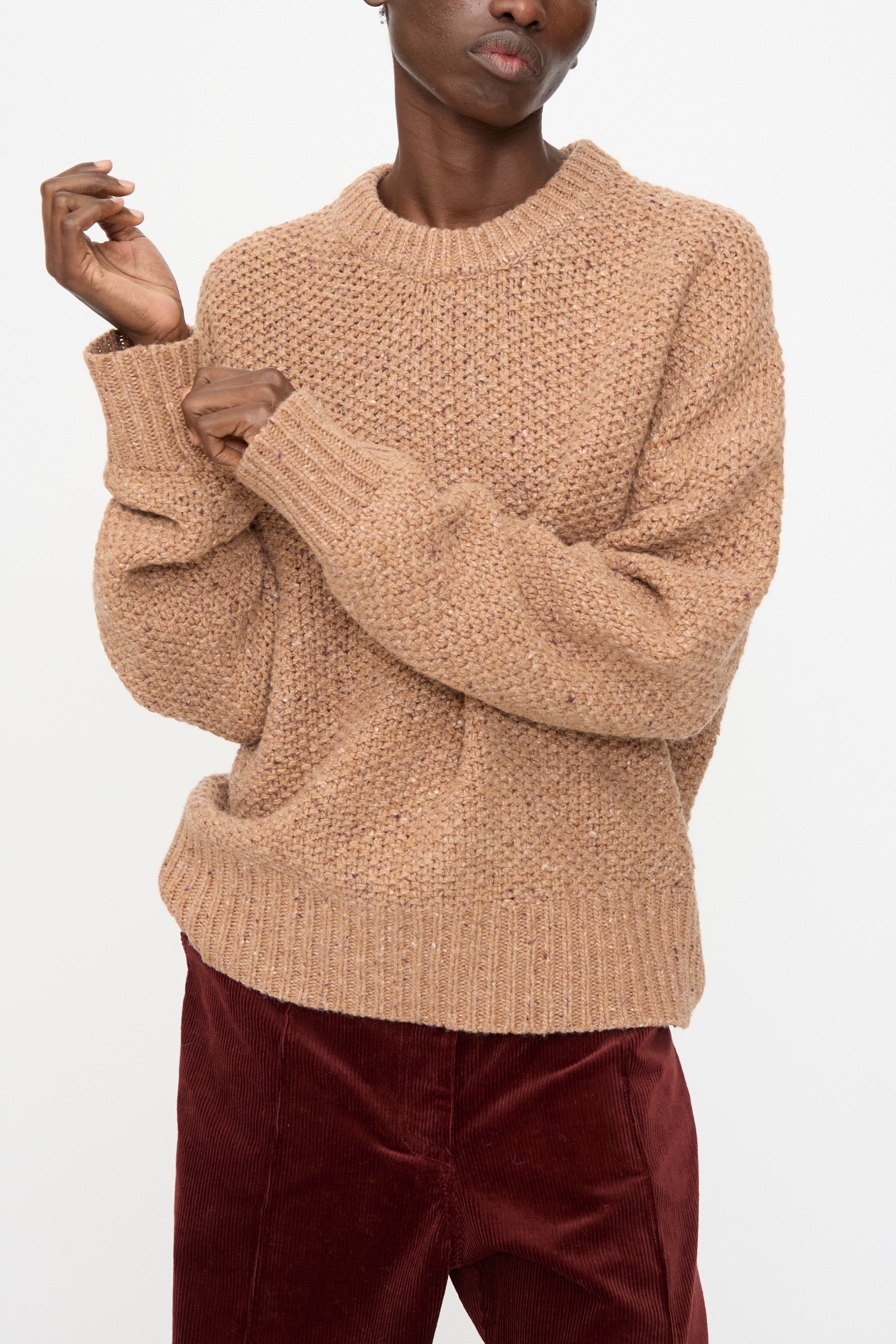 Model wears the Rachel Comey Prescot Sweater in Caramel, paired with burgundy corduroy pants, standing against a plain white background.