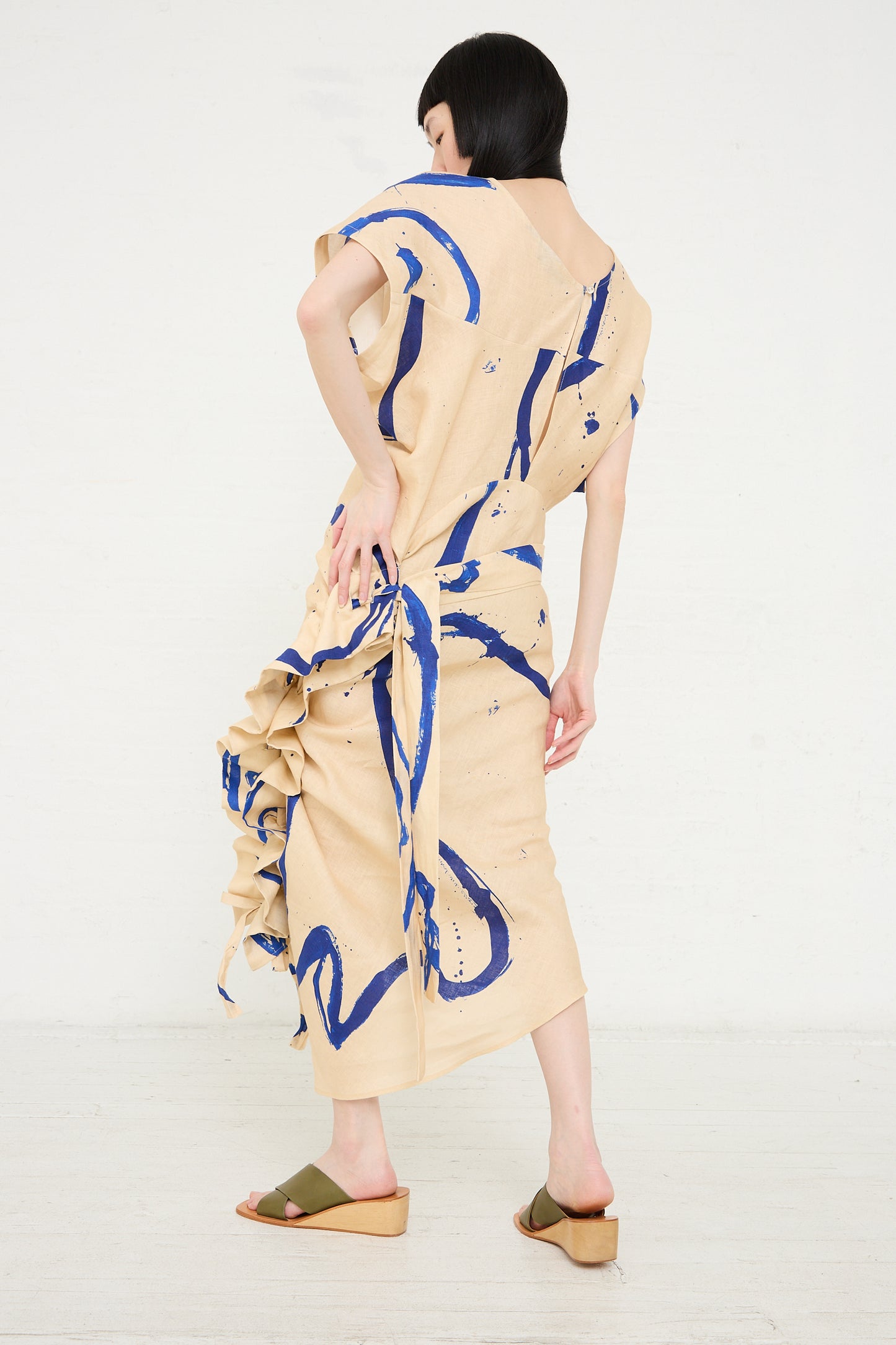 A woman models a Rachel Comey Regent Dress in Blush, with abstract printed linen patterns, viewed from behind.