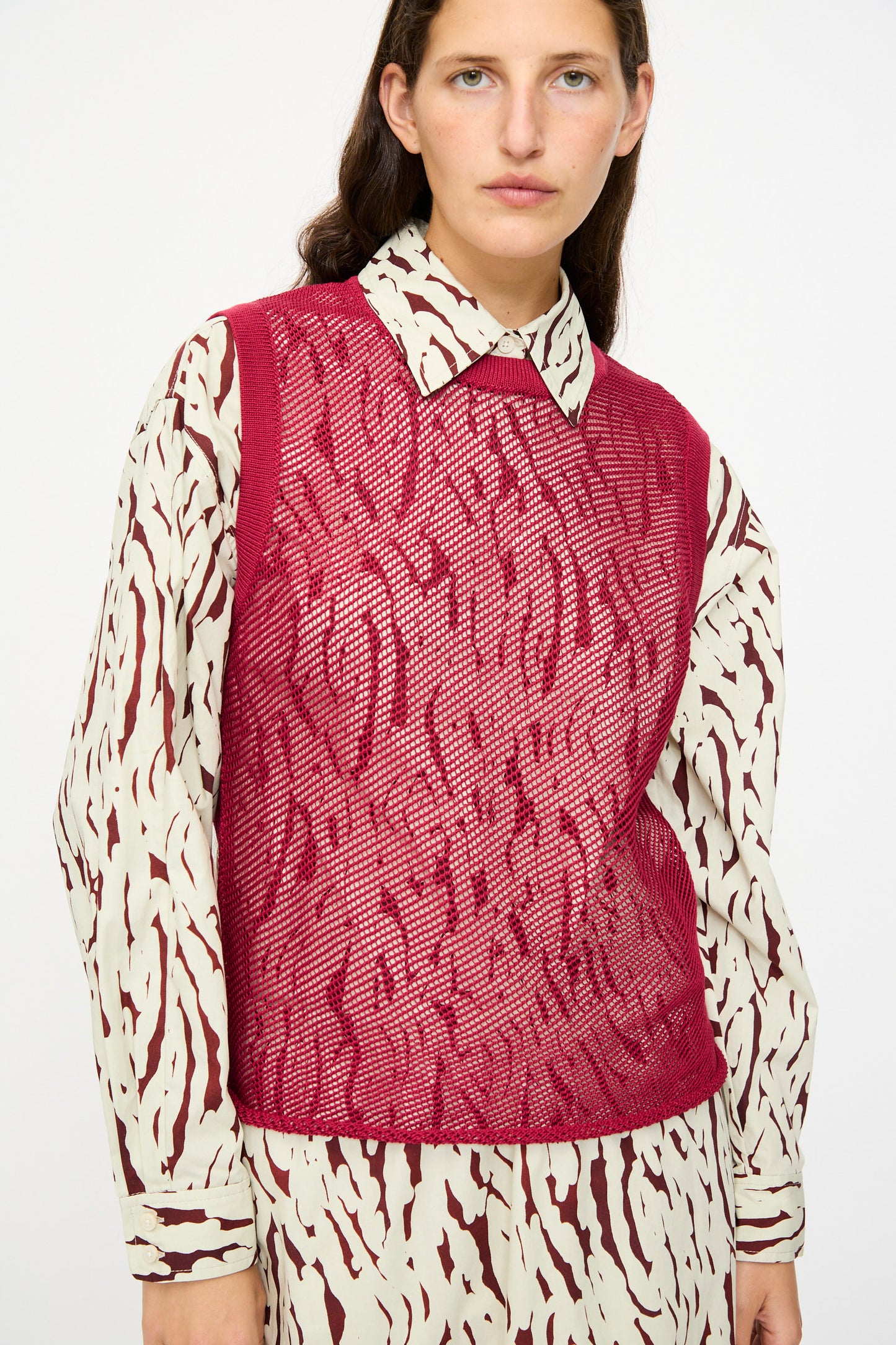 A person wears the Rachel Comey Rhett Tank in Deep Red, paired with a cream and burgundy patterned shirt and skirt, standing against a plain background.