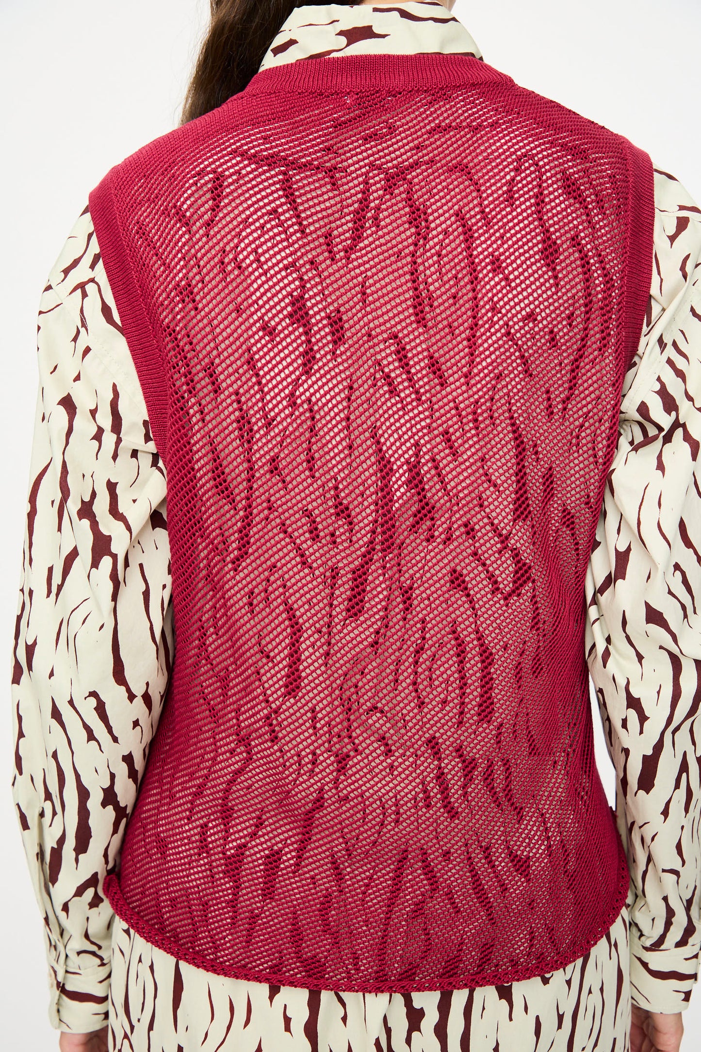 A person is seen from behind wearing the Rachel Comey Rhett Tank in Deep Red over a long-sleeve, abstract patterned shirt.