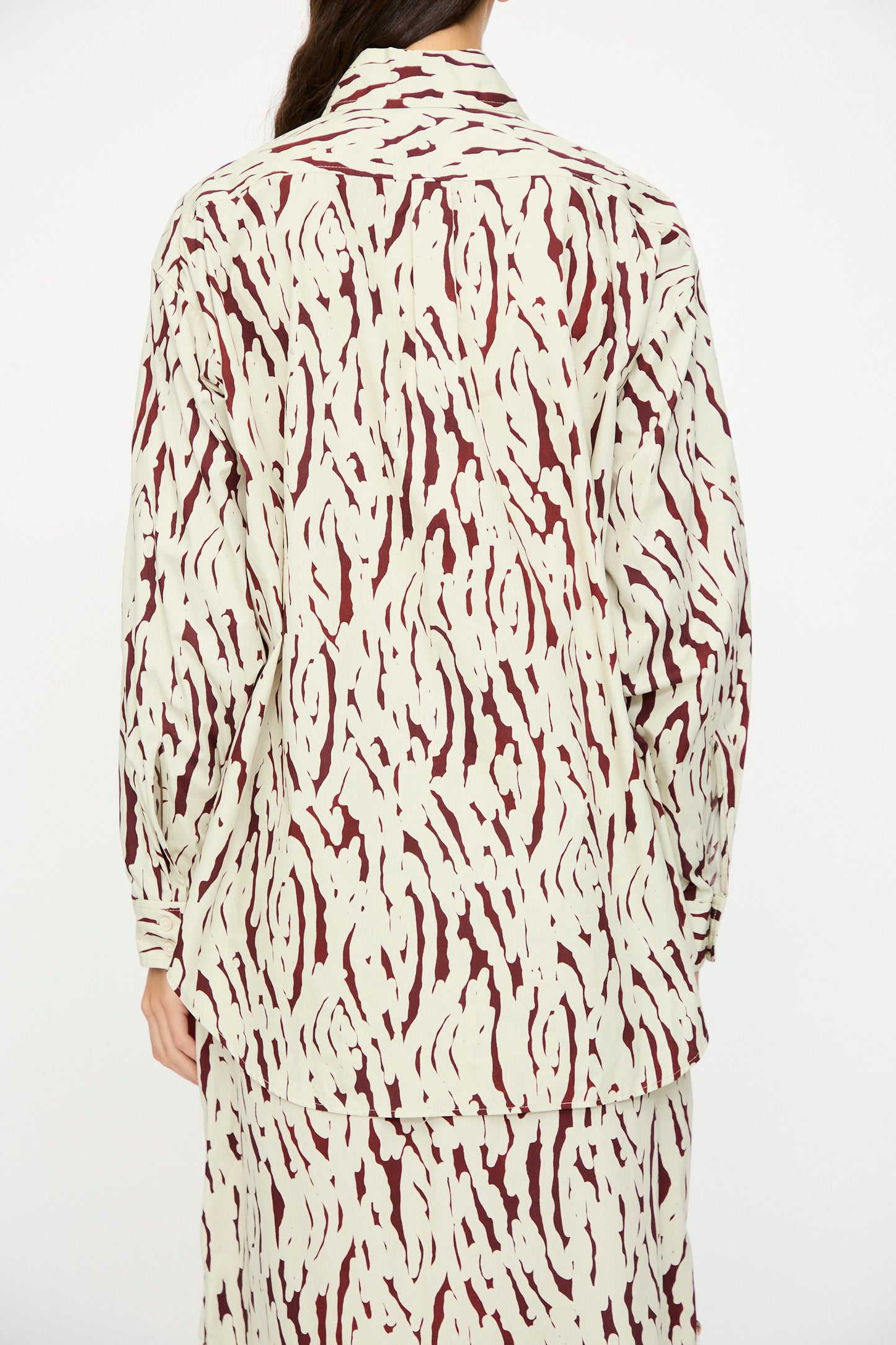 A person wearing the Rachel Comey Risa Top in Cream, featuring a maroon abstract Tiikeri print, is photographed from the back against a plain background.