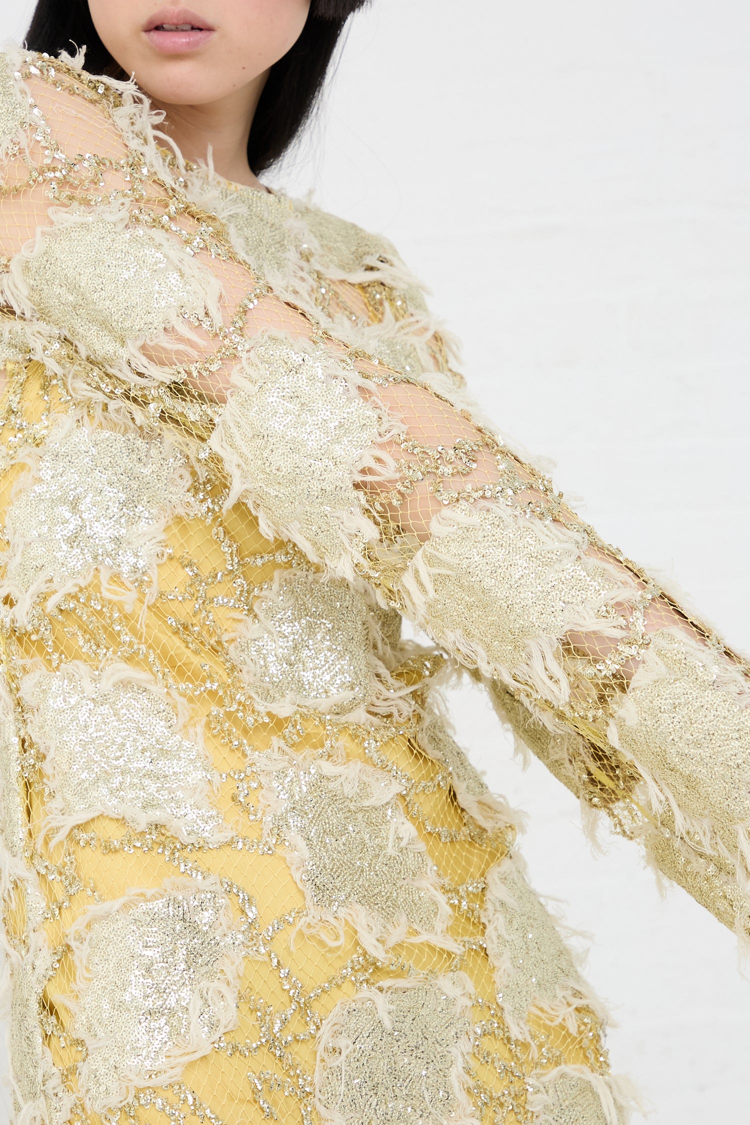 A close-up of a woman in a Rachel Comey Silla Dress in Gold with fringe details.