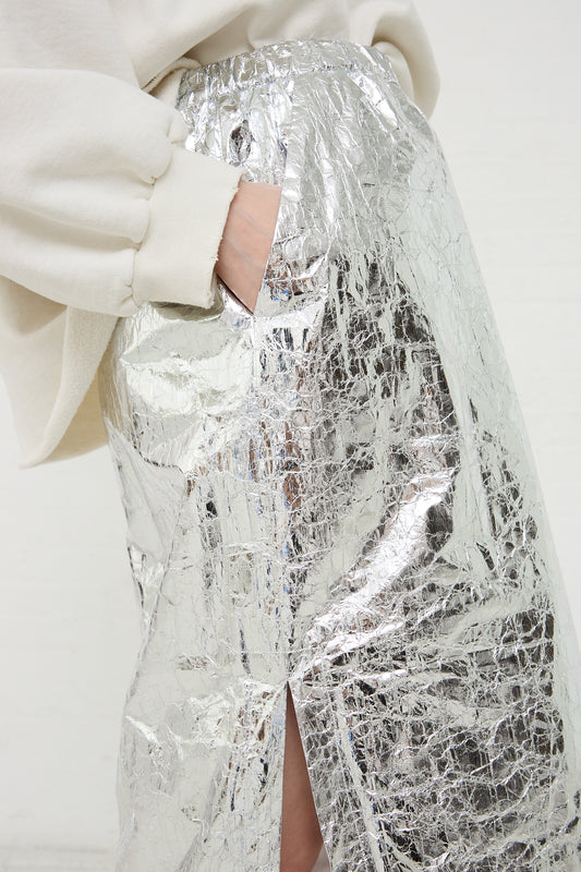 A person wearing a Rachel Comey Mott Skirt in Silver with a cream-colored top, resting a hand in the pocket.