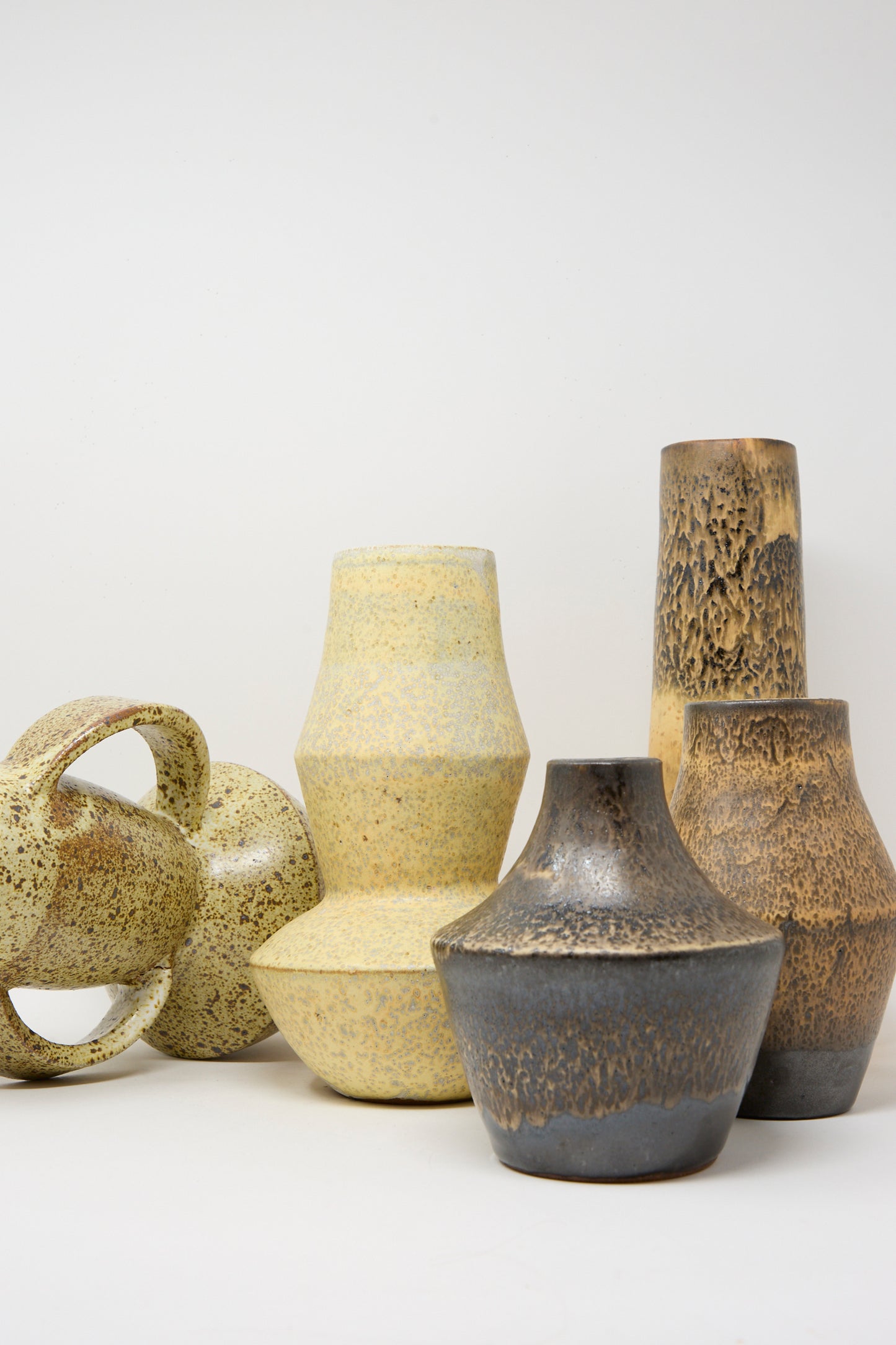 The Rachel Craven Shaped Vase in Eggshell Speckle is featured among six ceramic vases and vessels in neutral tones with varied textures and shapes, all arranged against a plain white background.