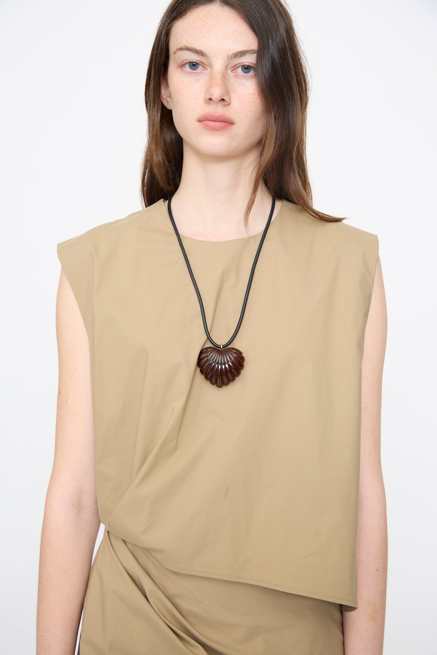 A woman with long brown hair wears a sleeveless beige top and the Rachel Comey Findon Necklace in Dark Tortoise. She stands against a plain white background.