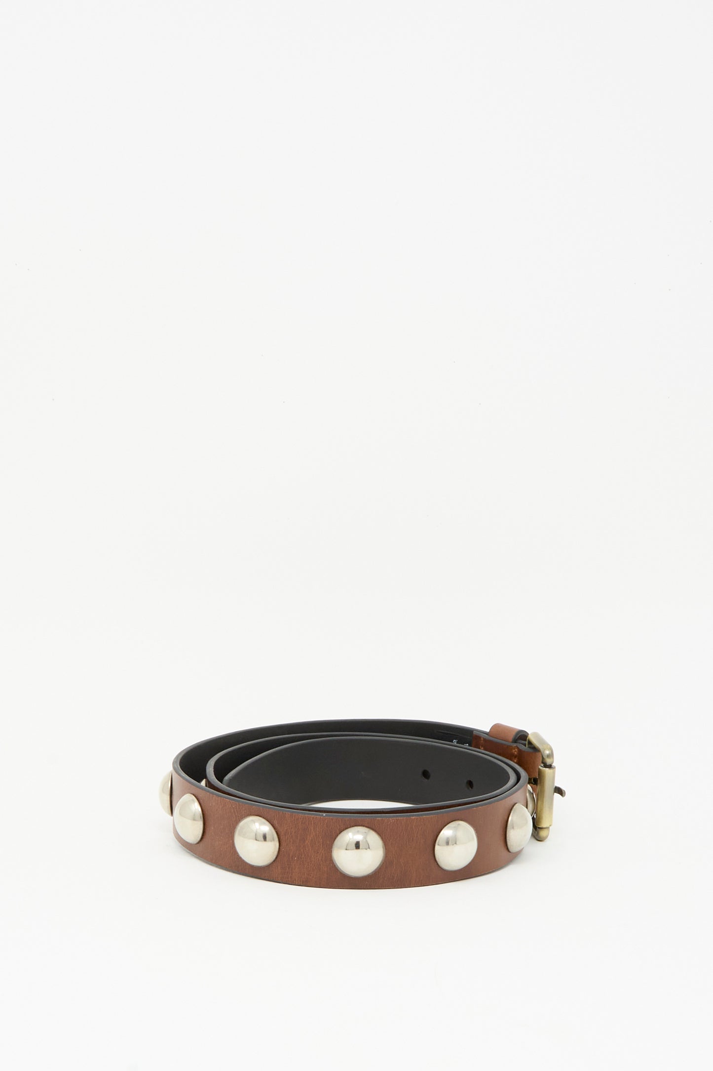 The Rachel Comey Studded Belt in Saddle is a dark brown leather belt featuring large round silver studs and a bronze buckle, coiled neatly on a plain white background.