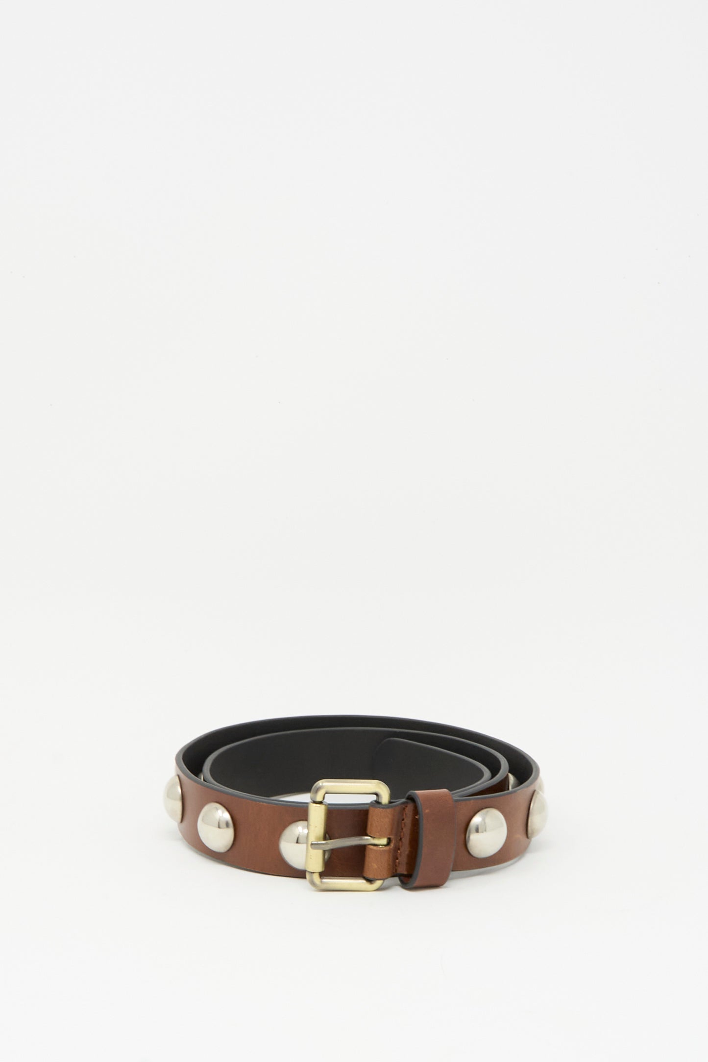 The Rachel Comey Studded Belt in Saddle, featuring a dark brown leather strap with large silver studs and a bronze buckle, is coiled neatly on a plain white background.