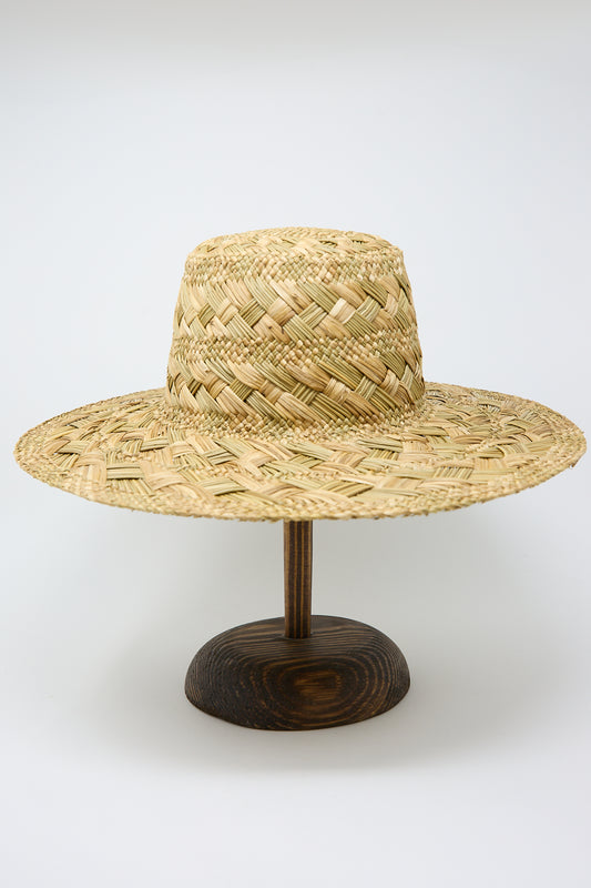 A wide-brimmed Treccia Lai Straw Hat in Natural displayed on a wooden stand against a plain white background by Reinhard Plank.