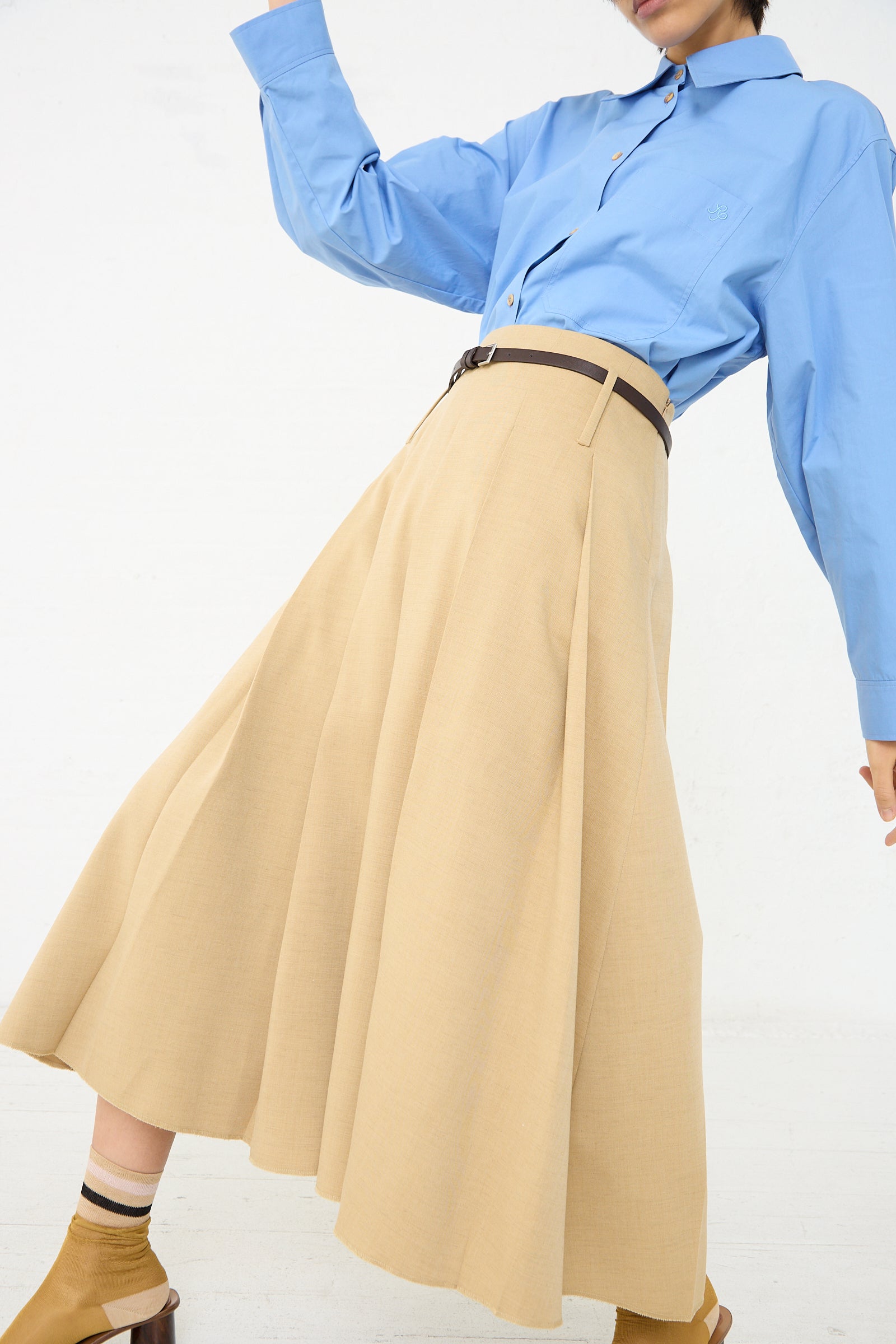 A woman in a blue shirt and Rejina Pyo's Odette Skirt in Beige. Front view. 