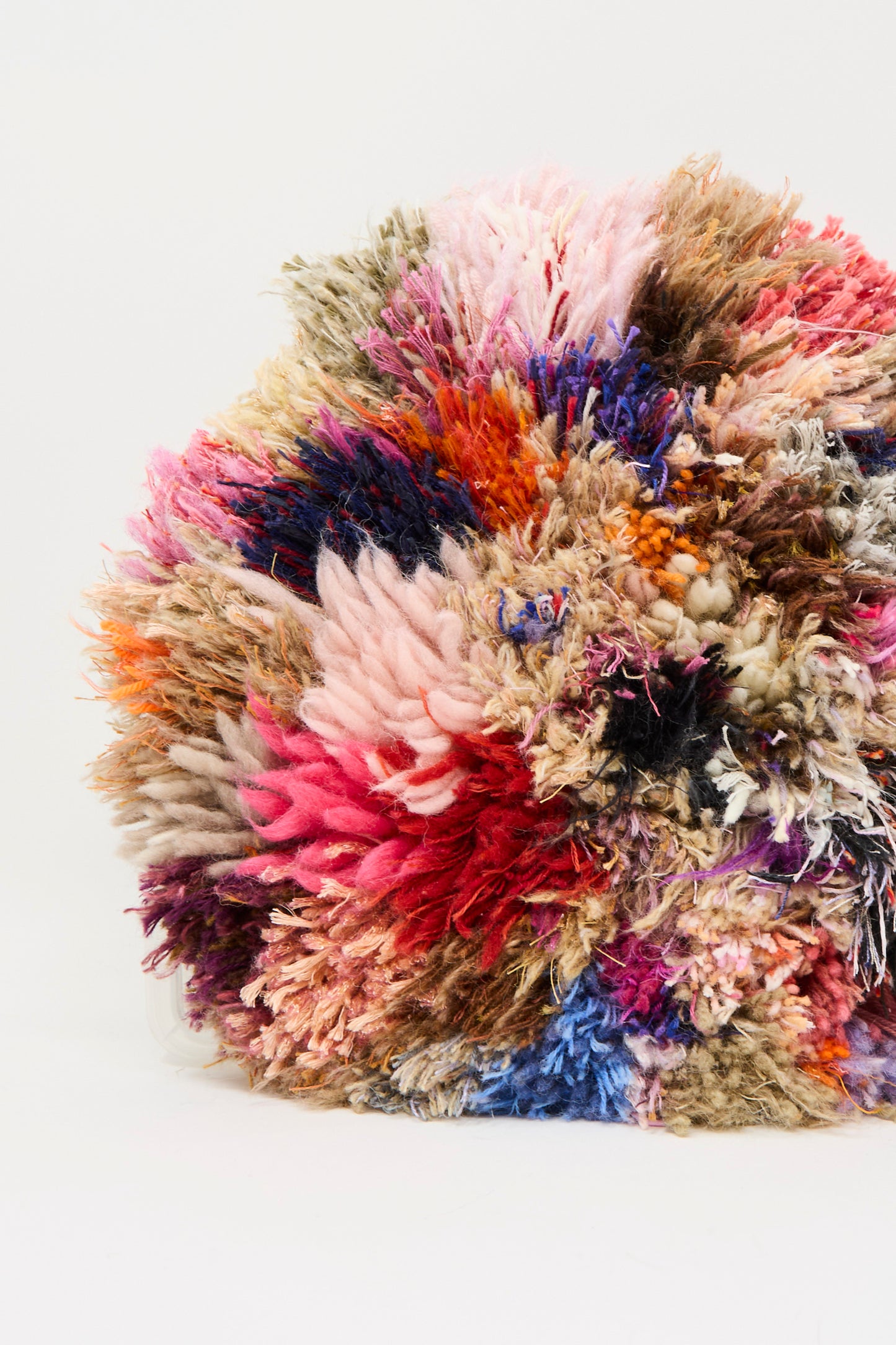 A close-up of the Handmade Cushion in Multi I by Renilde De Peuter shows its textured, multicolored surface with pink, blue, brown, orange, and cream hues against a plain white background.
