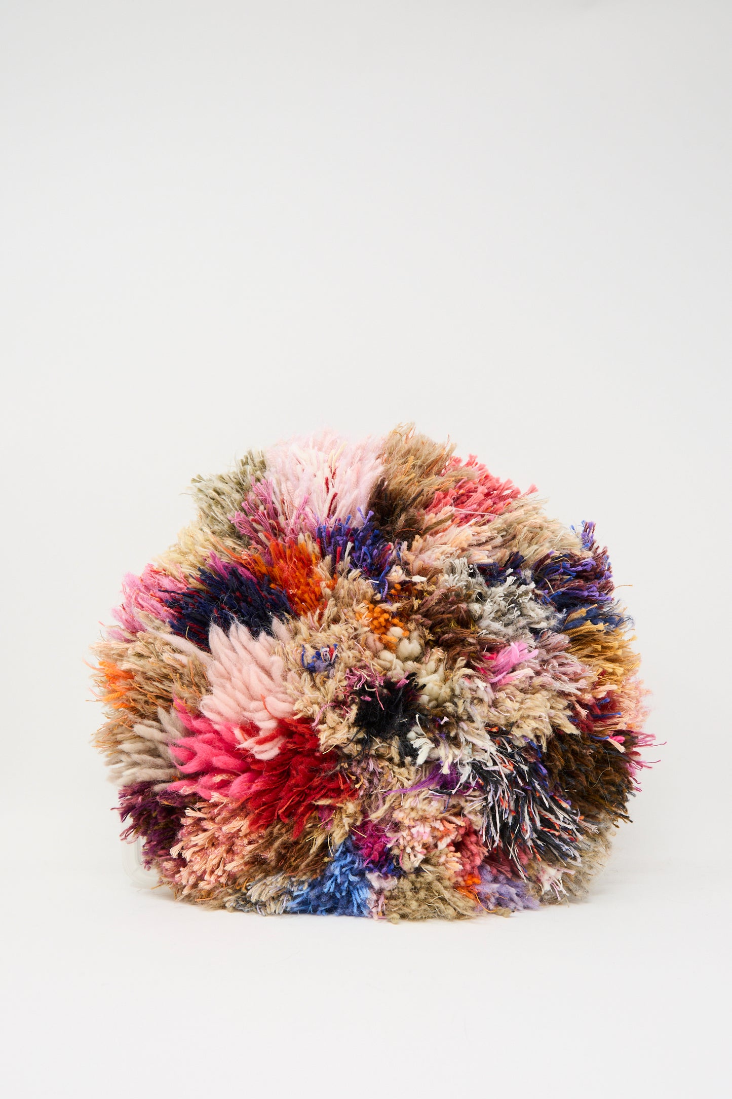 The "Handmade Cushion in Multi I" by Renilde De Peuter features a dense, round cluster of multicolored yarn, displayed against a plain white background.