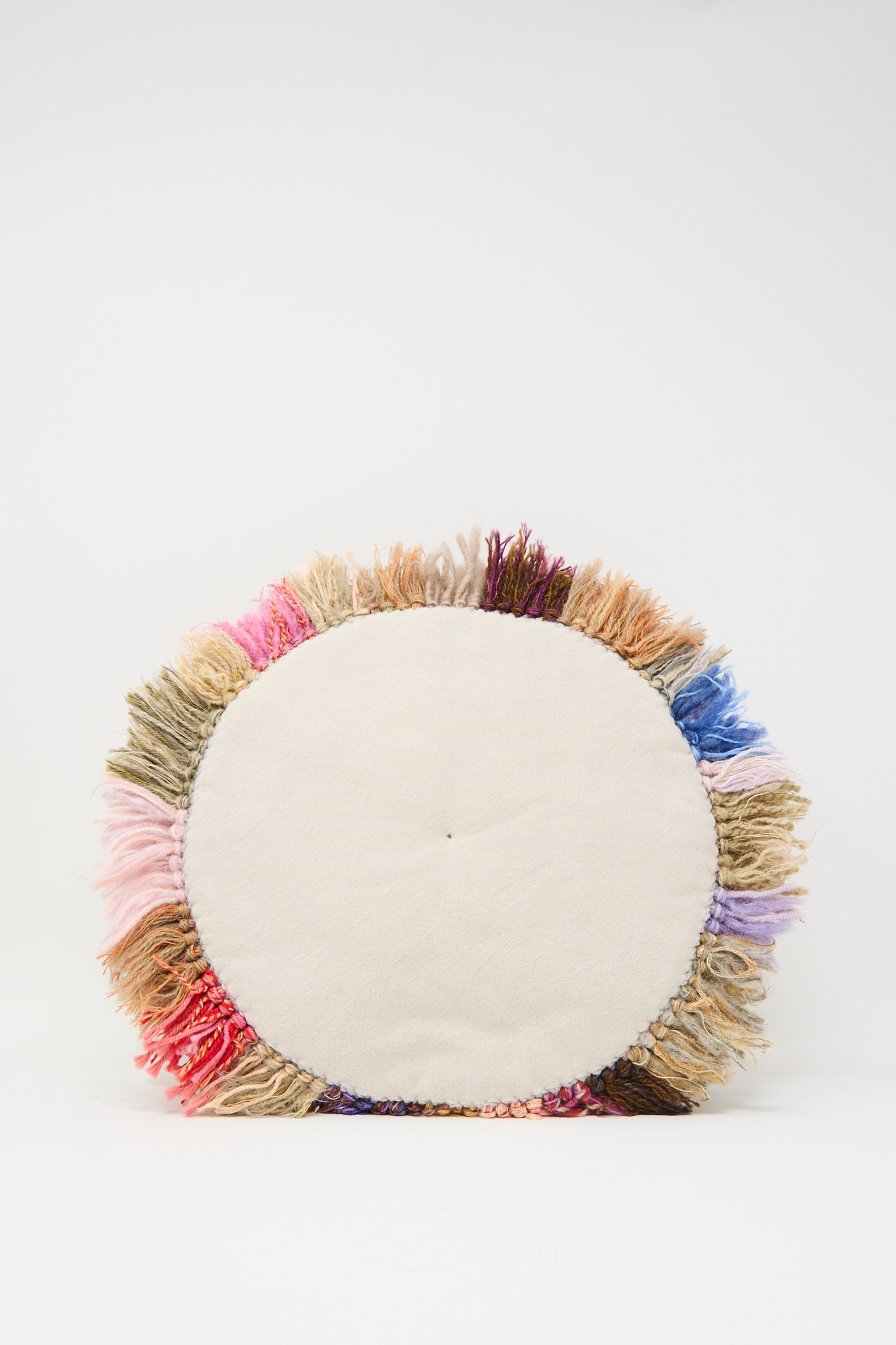 The Handmade Cushion in Multi I by Renilde De Peuter is a round, white seat cushion with multicolored fringe, crafted from colorful fabrics and displayed on a plain white background.