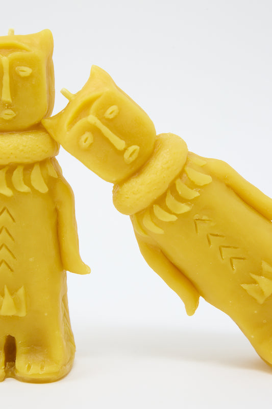 Two yellow Forest Goddess candles by Rinn to Hitsuji, shaped like intricately detailed human figures, standing facing each other on a white background.