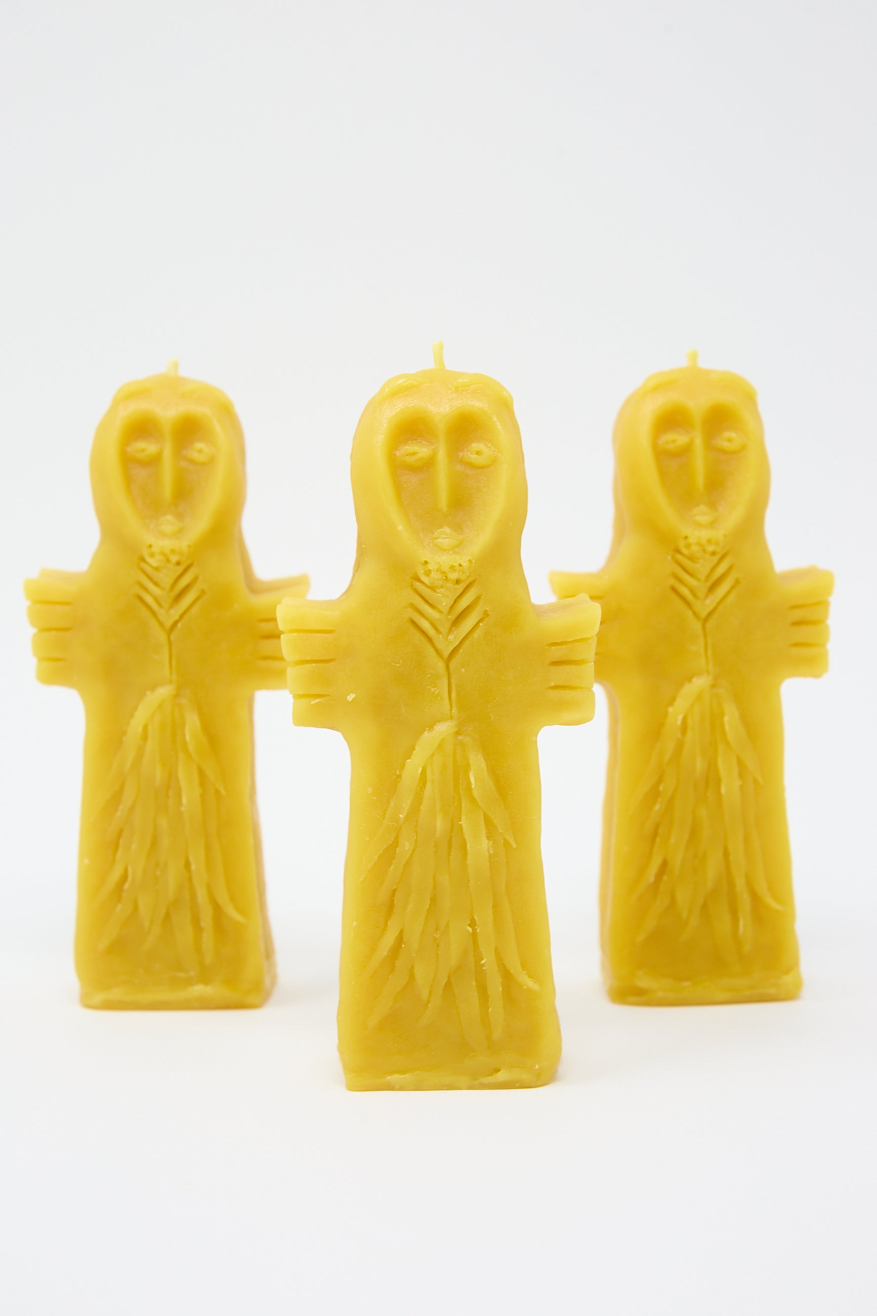 Three yellow Sky Goddess Candles from Rinn to Hitsuji, shaped like figures with cloaked bodies and serene facial expressions, standing upright against a white background.