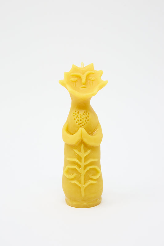 A yellow, sculpted Sun Goddess Candle in the shape of a tree with a face, featuring textured leaves and sun motifs, made from Japanese soy wax, set against a plain white background by Rinn to Hitsuji.