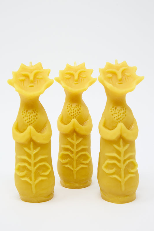 Three "Sun Goddess" candles shaped like figures with sun faces, body patterns resembling leaves, all standing upright on a white background by Rinn to Hitsuji.