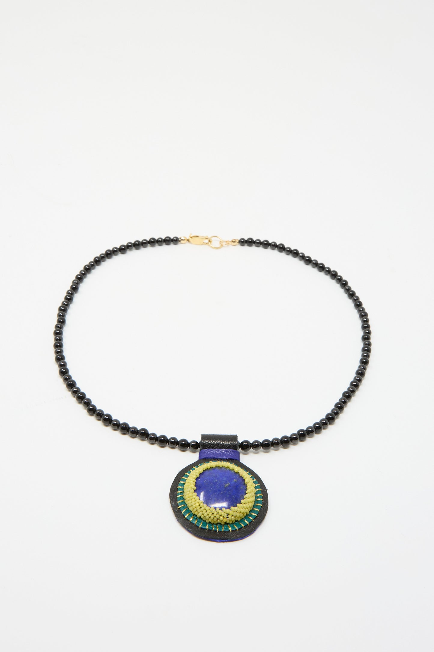 Introducing the Charm Necklace by Robin Mollicone—an handmade piece that showcases a unique beaded design highlighted by a circular pendant with intricate blue and green embroidery set against a black background, perfectly complemented by an elegant Black Onyx charm.