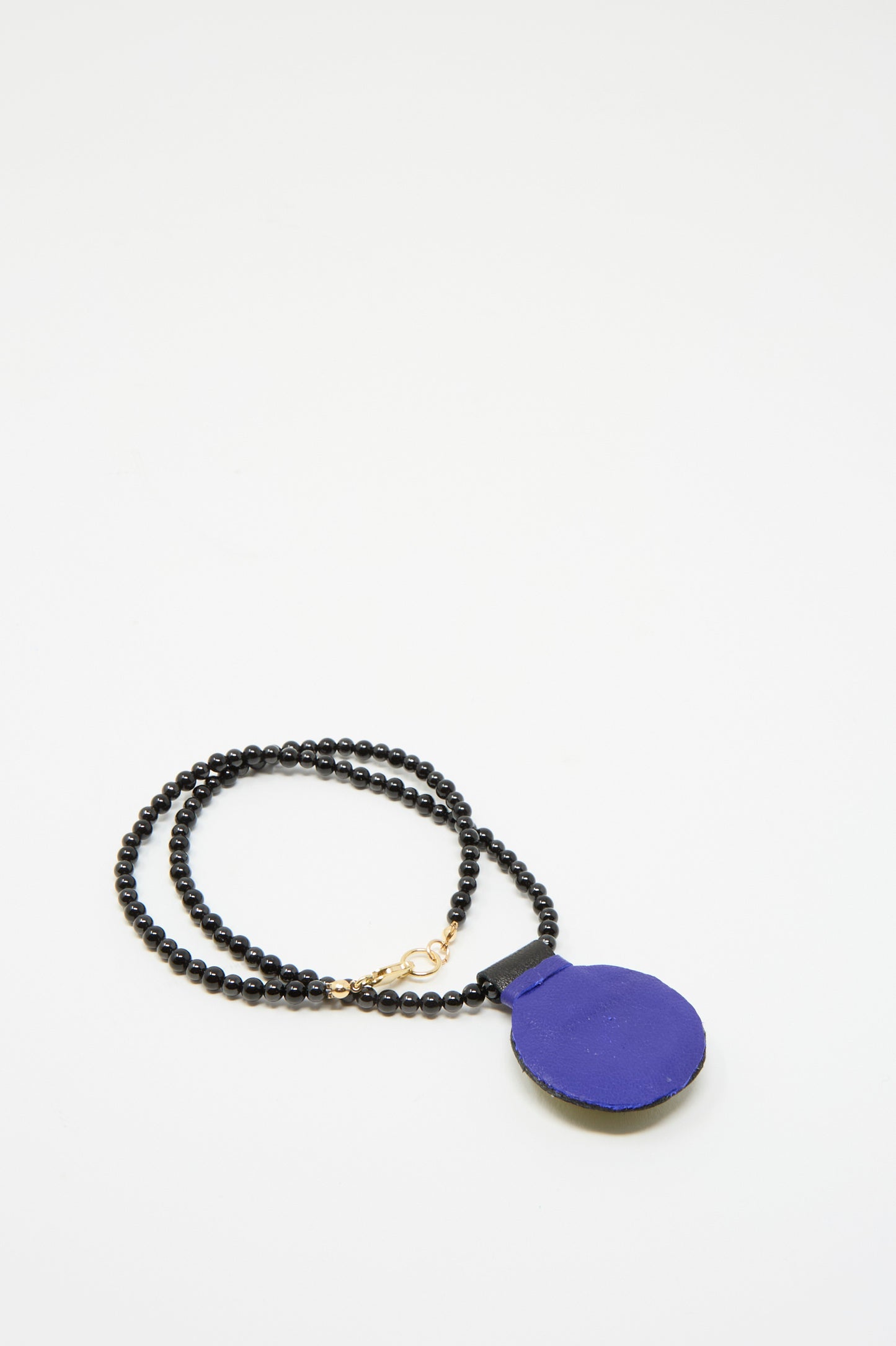 A Charm Necklace by Robin Mollicone viewed facing down, showcasing Onyx beads and a flat round blue Lapis charm pendant on a white backdrop.