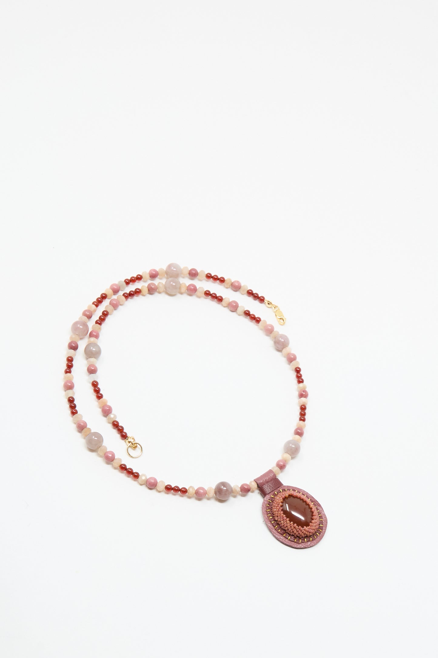 The Robin Mollicone Love Bead Necklace in Pink with Carnelian Charm features alternating pink and red vintage glass beads and a round pink pendant with a central oval stone, shown on a white background.