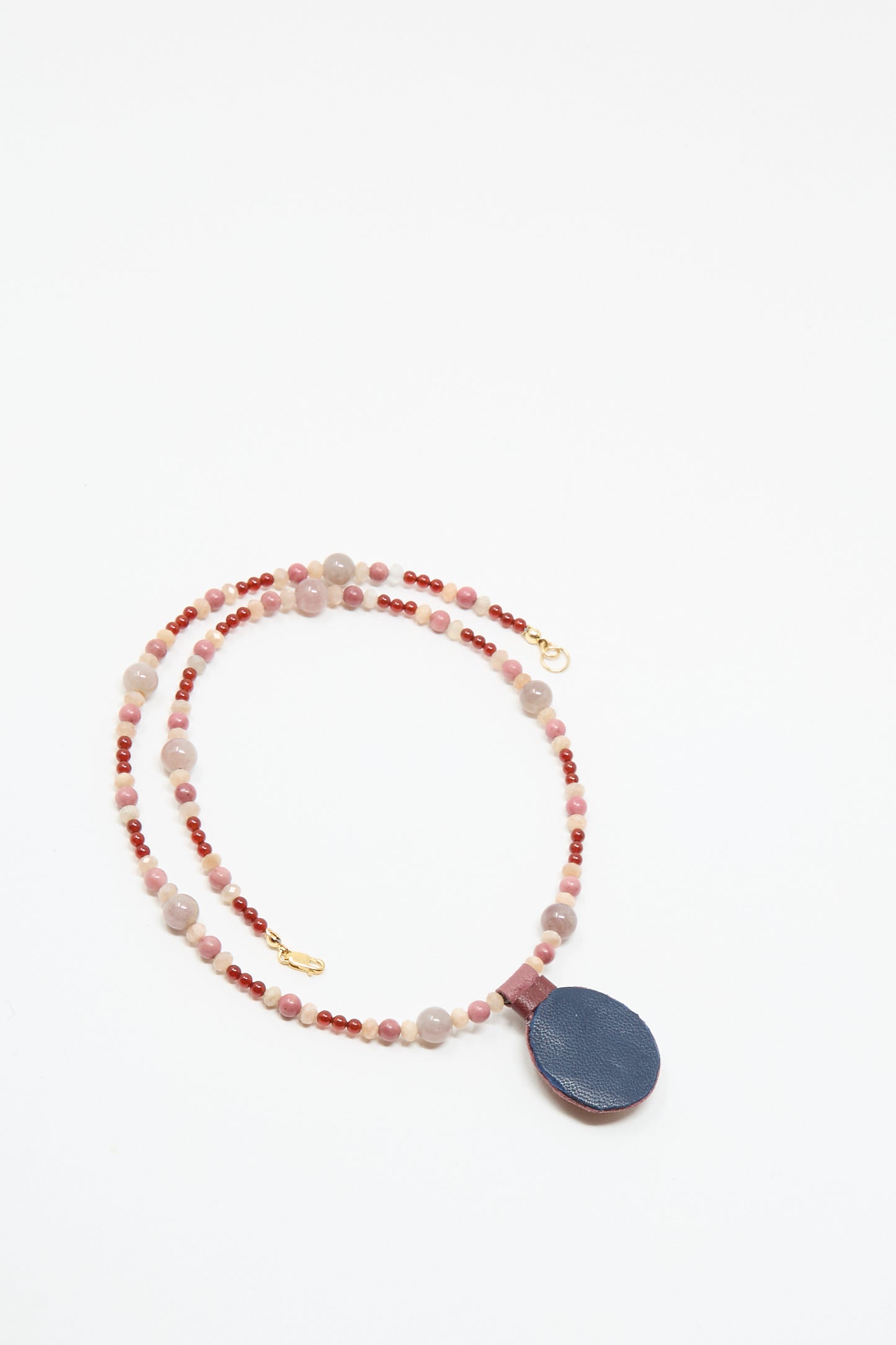 The Robin Mollicone Love Bead Necklace in Pink with Carnelian Charm features vintage pink and red glass beads, a large round dark blue pendant, and gold clasp, displayed on a white background.