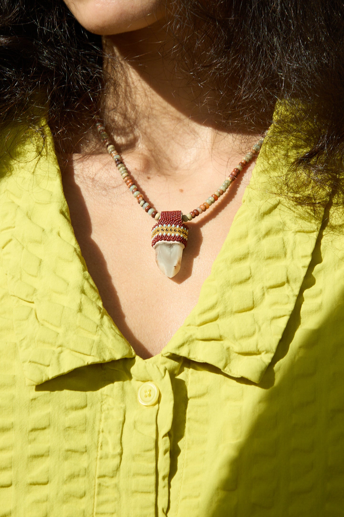 A person wearing a Pendulum Necklace adorned with Sea Sediment Imperial Jasper beads and Lithium Quartz, designed by Robin Mollicone.