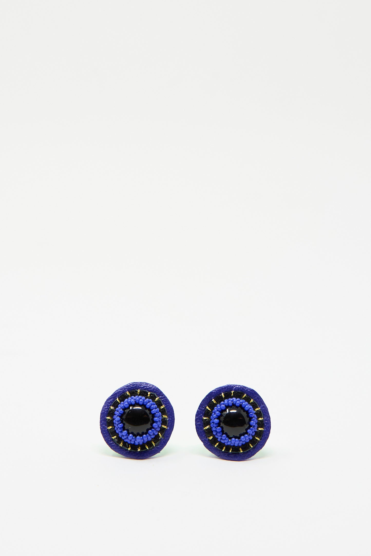 Introducing the Stud Earrings in Onyx by Robin Mollicone: these handcrafted, circular earrings feature a onyx center embellished with blue beads against a simple white backdrop.
