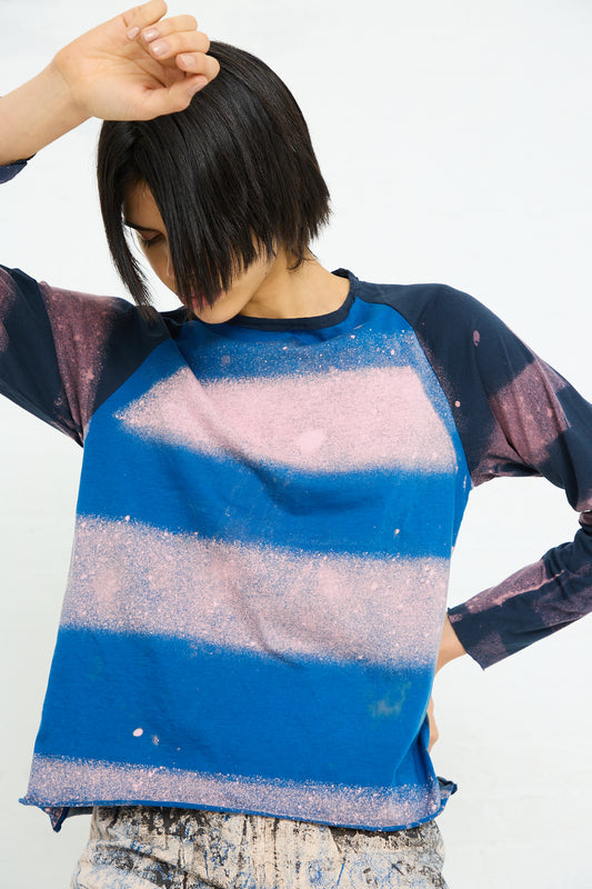 Person in a SC103 Cotton Jersey Nest Long Sleeve in Warf with mixed stripe print and paint-like texture lifting hair with one hand.