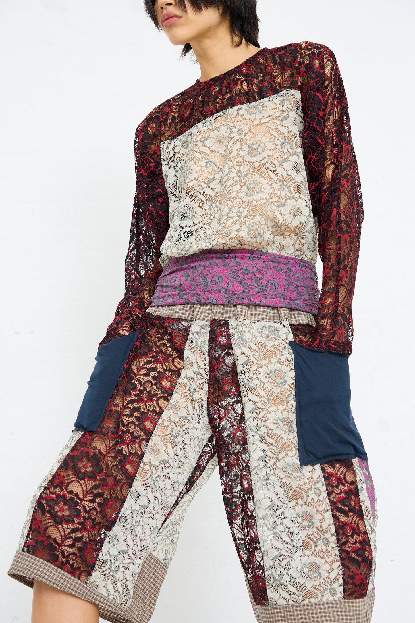 A person wearing an eclectic outfit featuring mixed patterns and textures, including a SC103 Lace Ritual Top in Thrash.