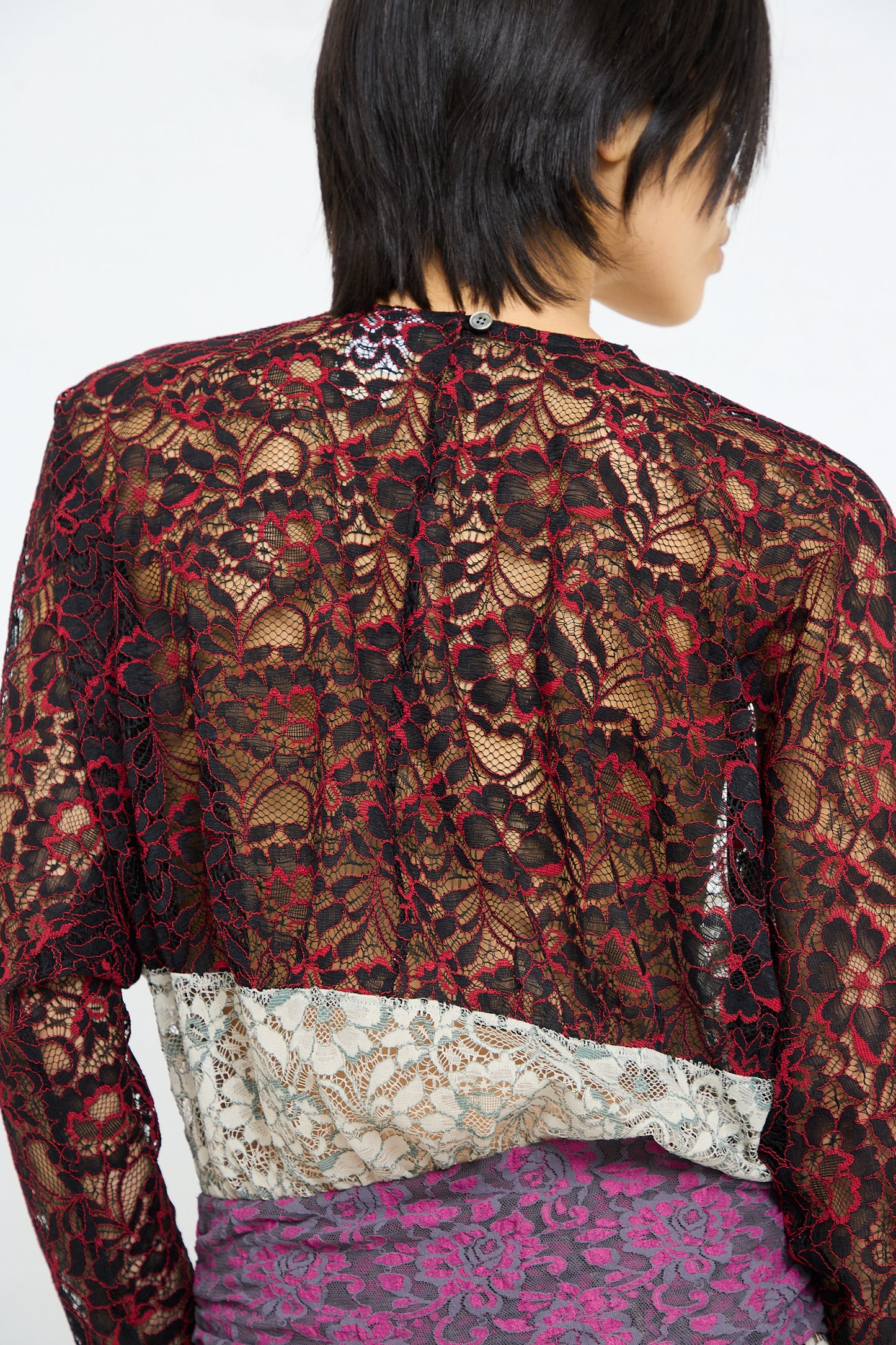A person wearing a SC103 Lace Ritual Top in Thrash with floral patterns, paired with a brightly patterned garment below.