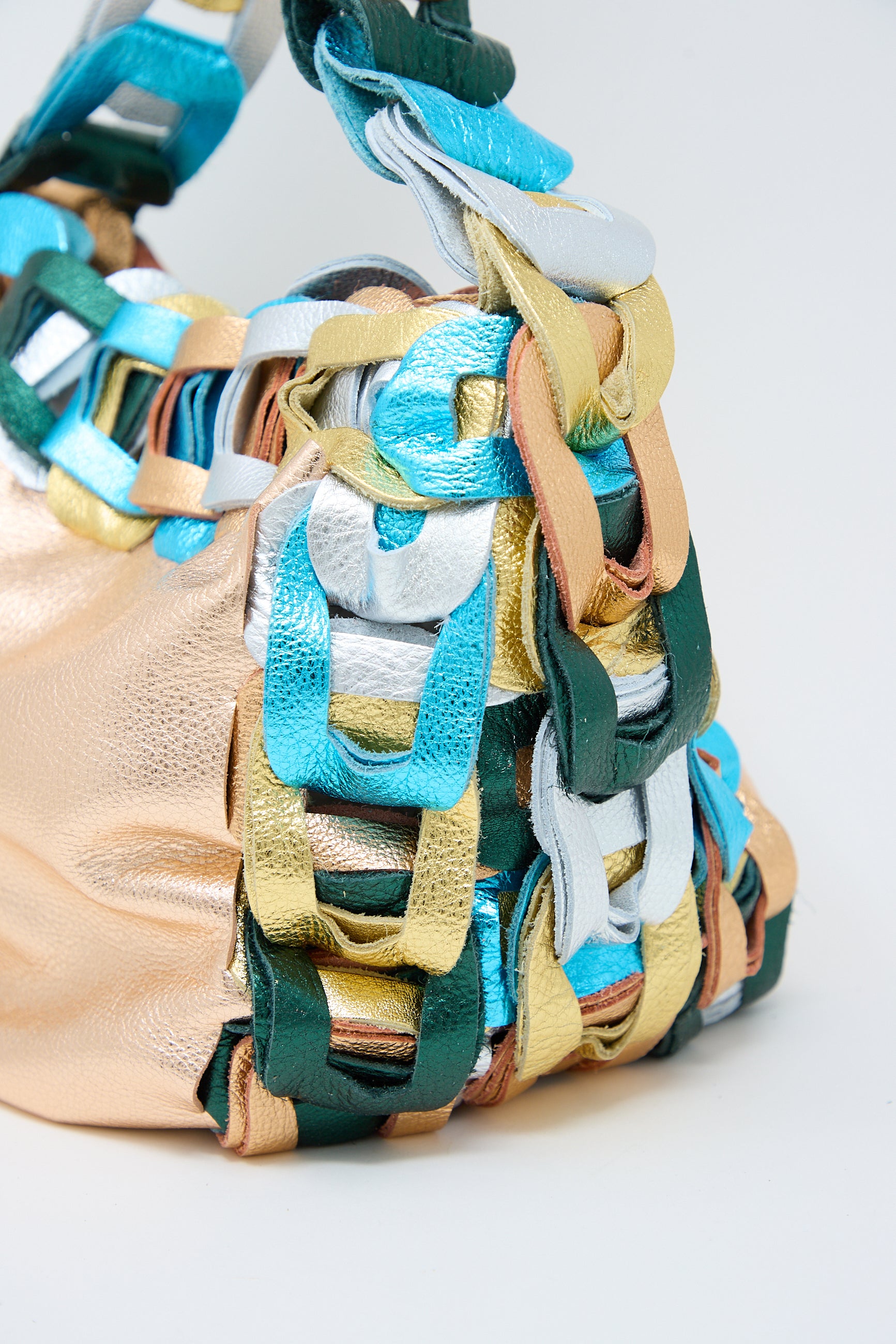 Close-up of a colorful SC103 Leather Drum Bag in Mineral featuring intertwined strips of metallic blue, green, gold, and silver leather with leather links strap.