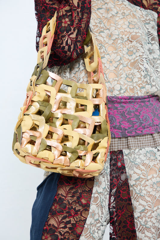 A person wearing a patchwork of various fabrics carries a unique SC103 handmade Leather Links Tote in Dew with pastel-colored bows.