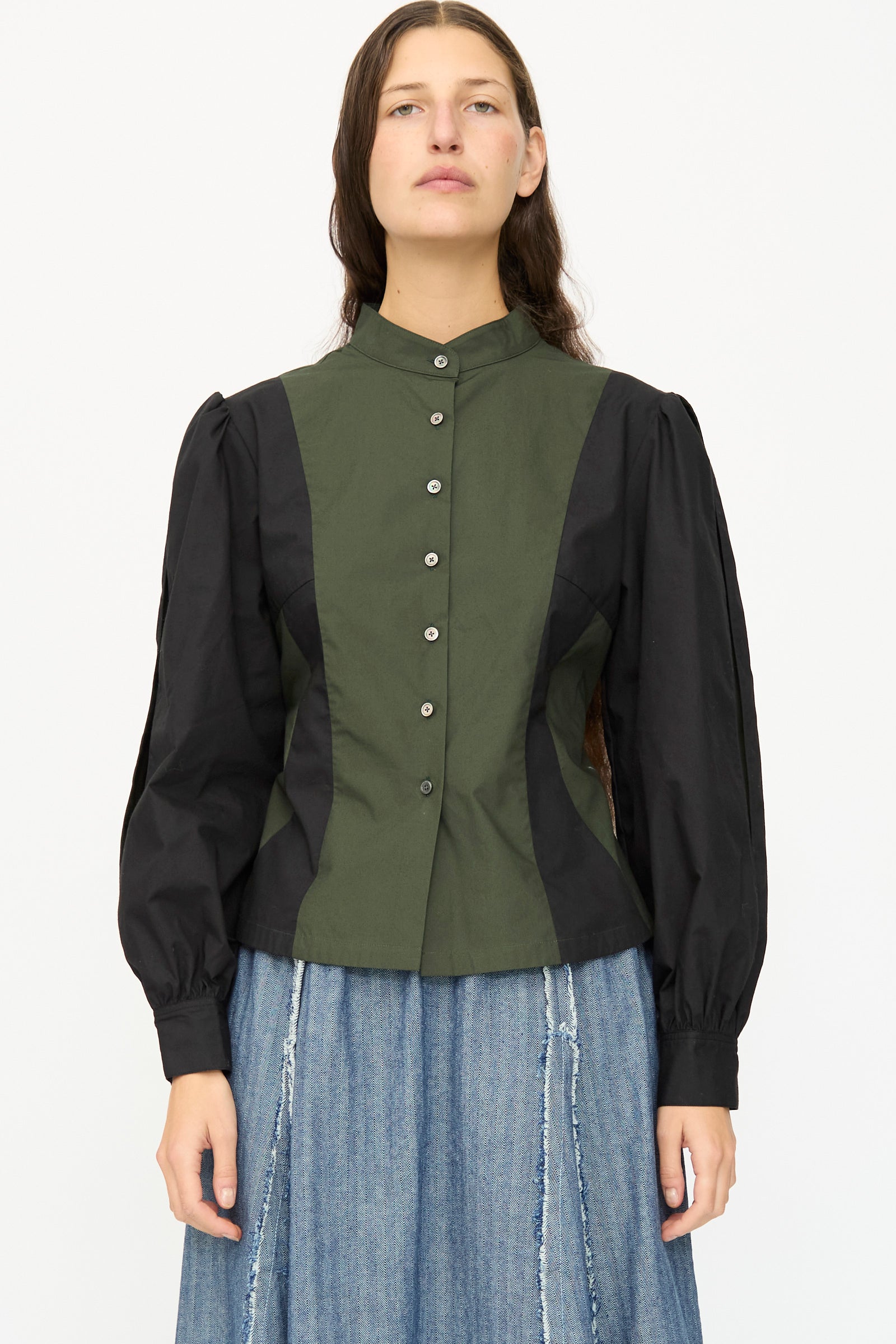 A person wears the SC103 Poplin Folio Blouse in Bolt—a color blocked cotton poplin top with bishop sleeves, high collar, and button front—paired with a blue denim skirt.