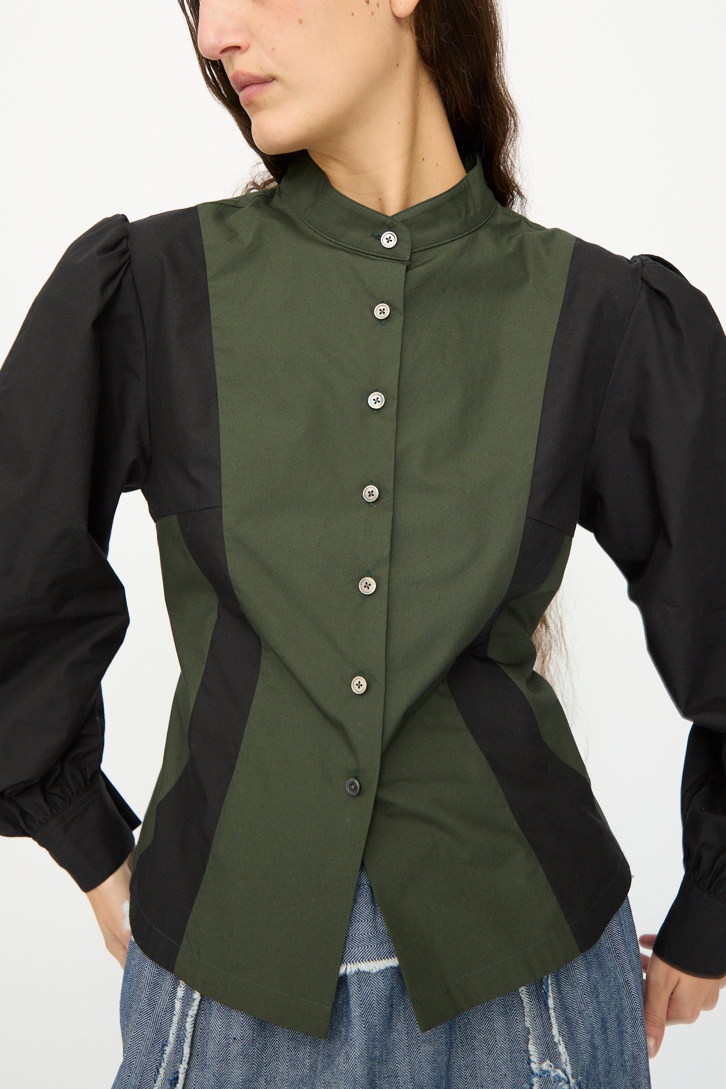 A person wearing the SC103 Poplin Folio Blouse in Bolt—green and black color-blocked cotton poplin with bishop sleeves—and blue denim pants, standing against a plain background.
