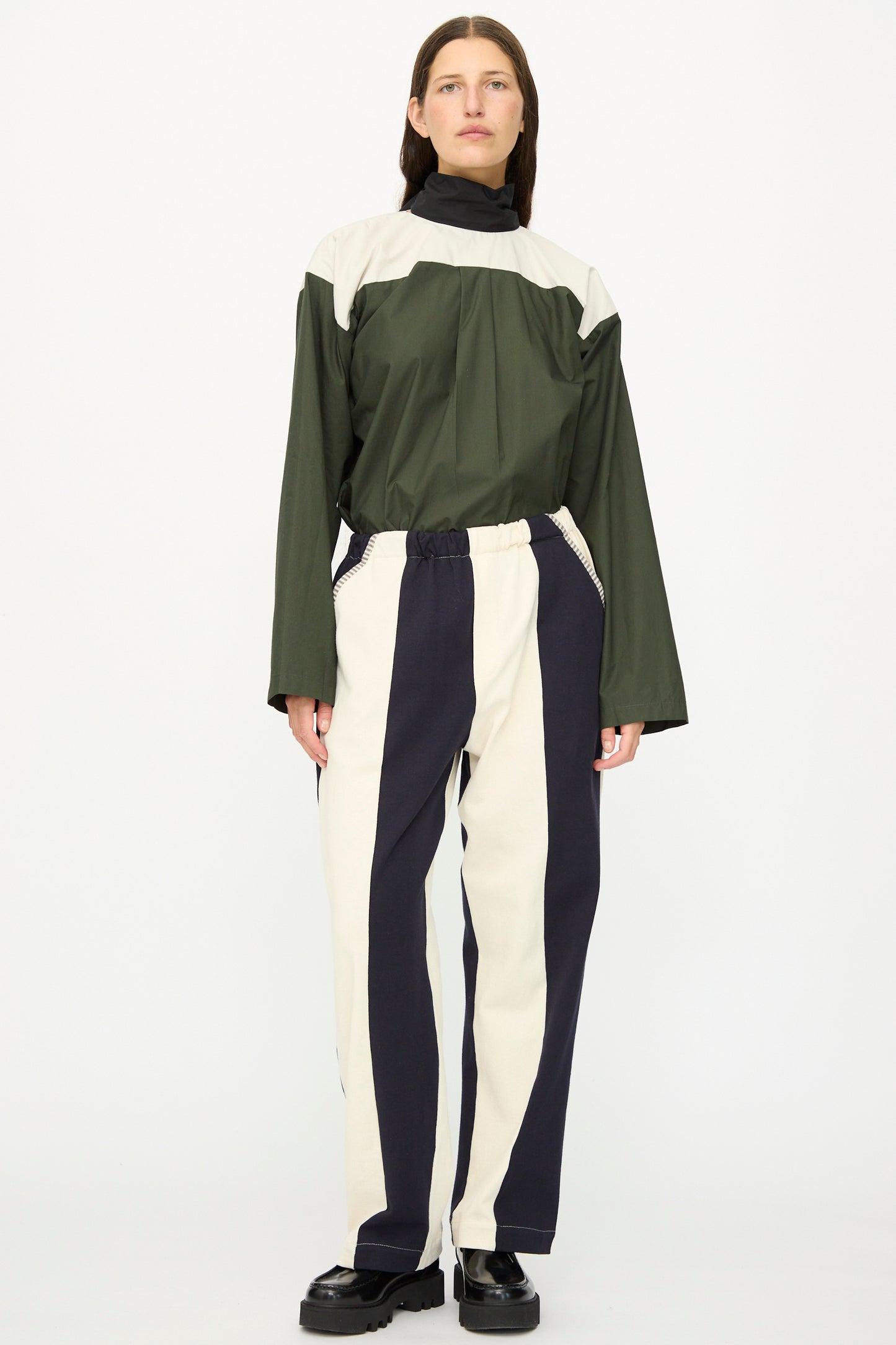 A person stands facing forward wearing SC103's Rib Knit Leap Sweats in Index—relaxed fit, vertically striped cotton knit pants—in black shoes against a plain white background.