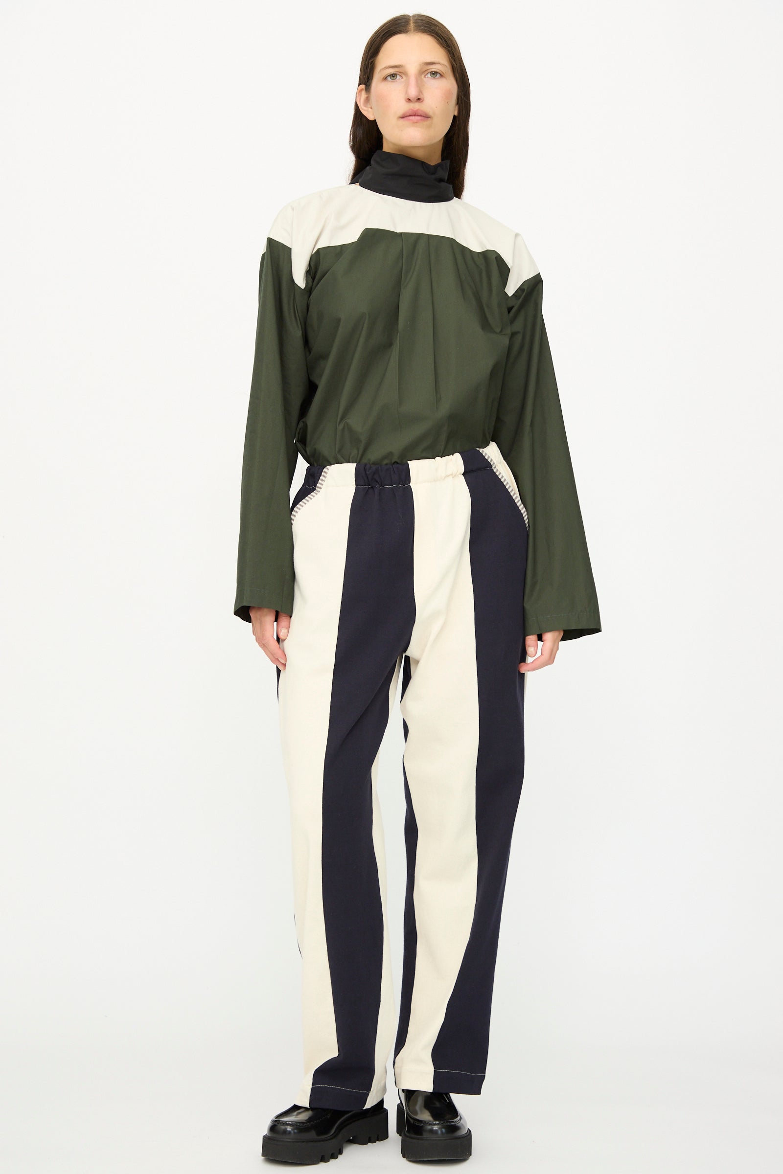A person stands facing forward wearing SC103's Rib Knit Leap Sweats in Index—relaxed fit, vertically striped cotton knit pants—in black shoes against a plain white background.