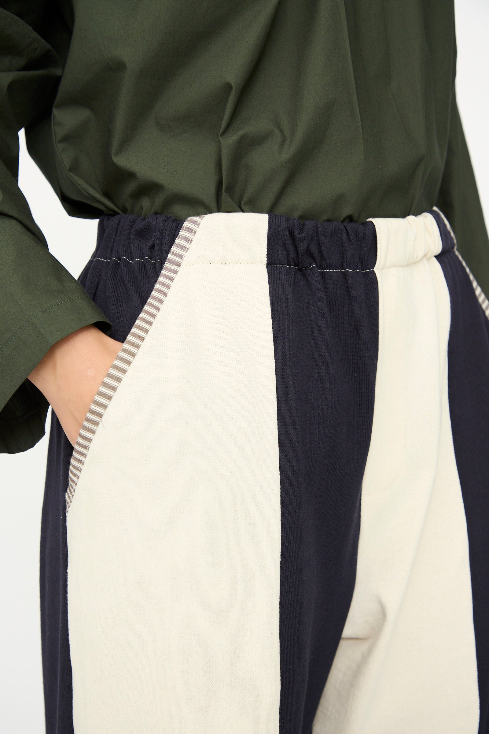 A person wearing SC103’s Rib Knit Leap Sweats in Index—high-waisted, relaxed fit pants in navy and cream with striped pocket trim—paired with a dark green top, made in NYC.