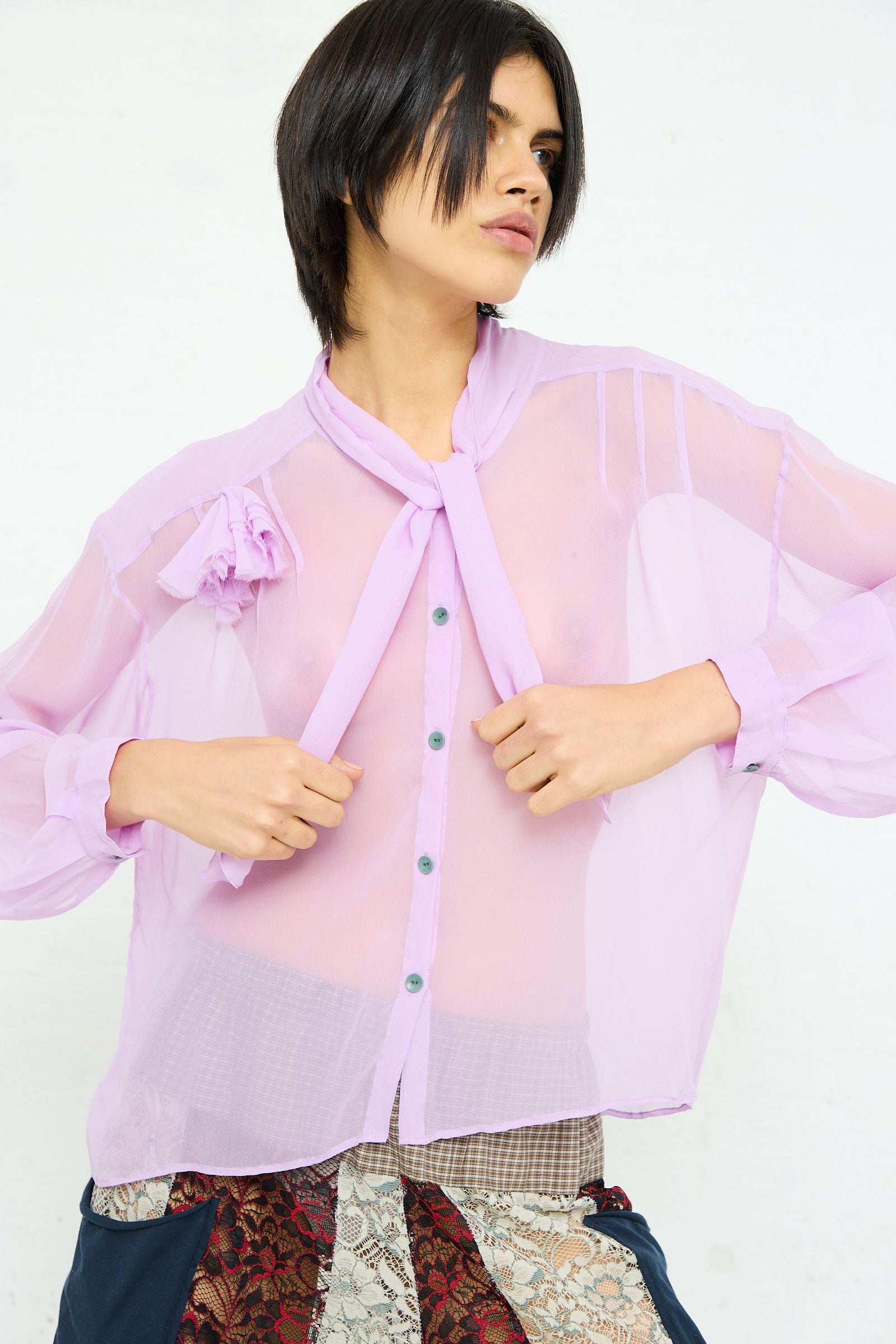 A person posing in a SC103 Silk Chiffon Mandolin Blouse in Sash with a tie at the neck, puffed sleeves, and rosette detail.